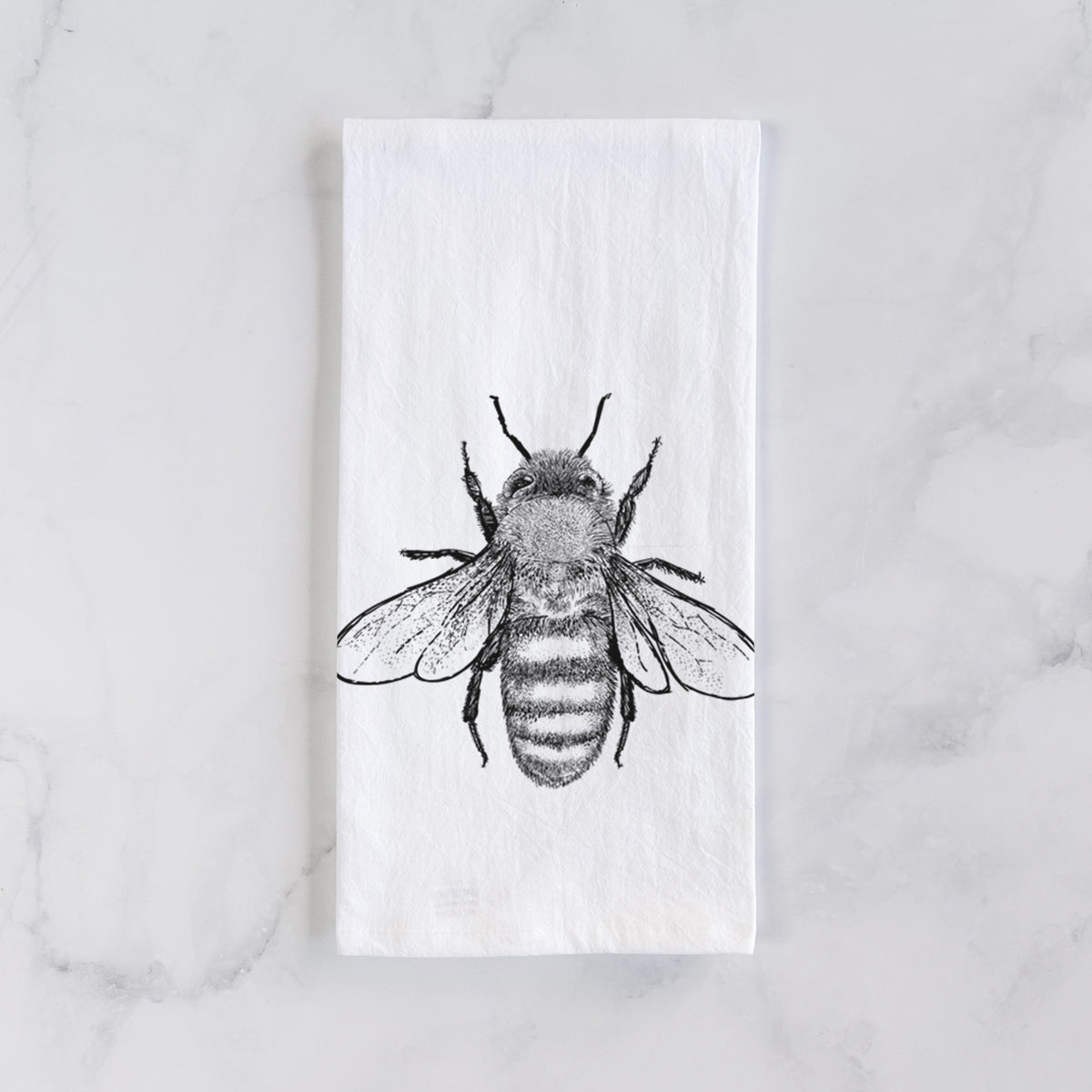 White cotton tea towel laid flat on marble, printed with a detailed black ink illustration of a honey bee with its wings spread, seen from above.