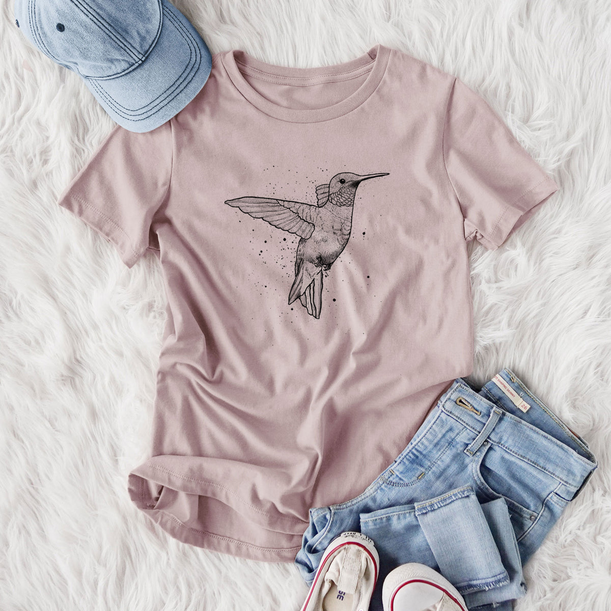 Women's relaxed fit cotton t-shirt printed with a black ink sketch of a ruby-throated hummingbird hovering with its wings raised, styled flat on a white faux fur rug with jeans.