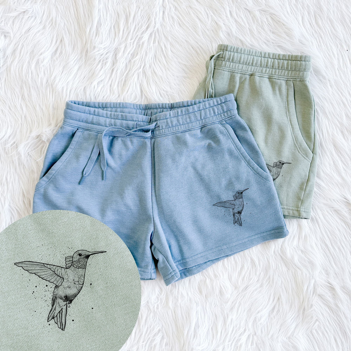 Two pairs of Cali Wave shorts in different colors printed with a black ink sketch of a ruby-throated hummingbird hovering with its wings raised, with a close-up of the print.