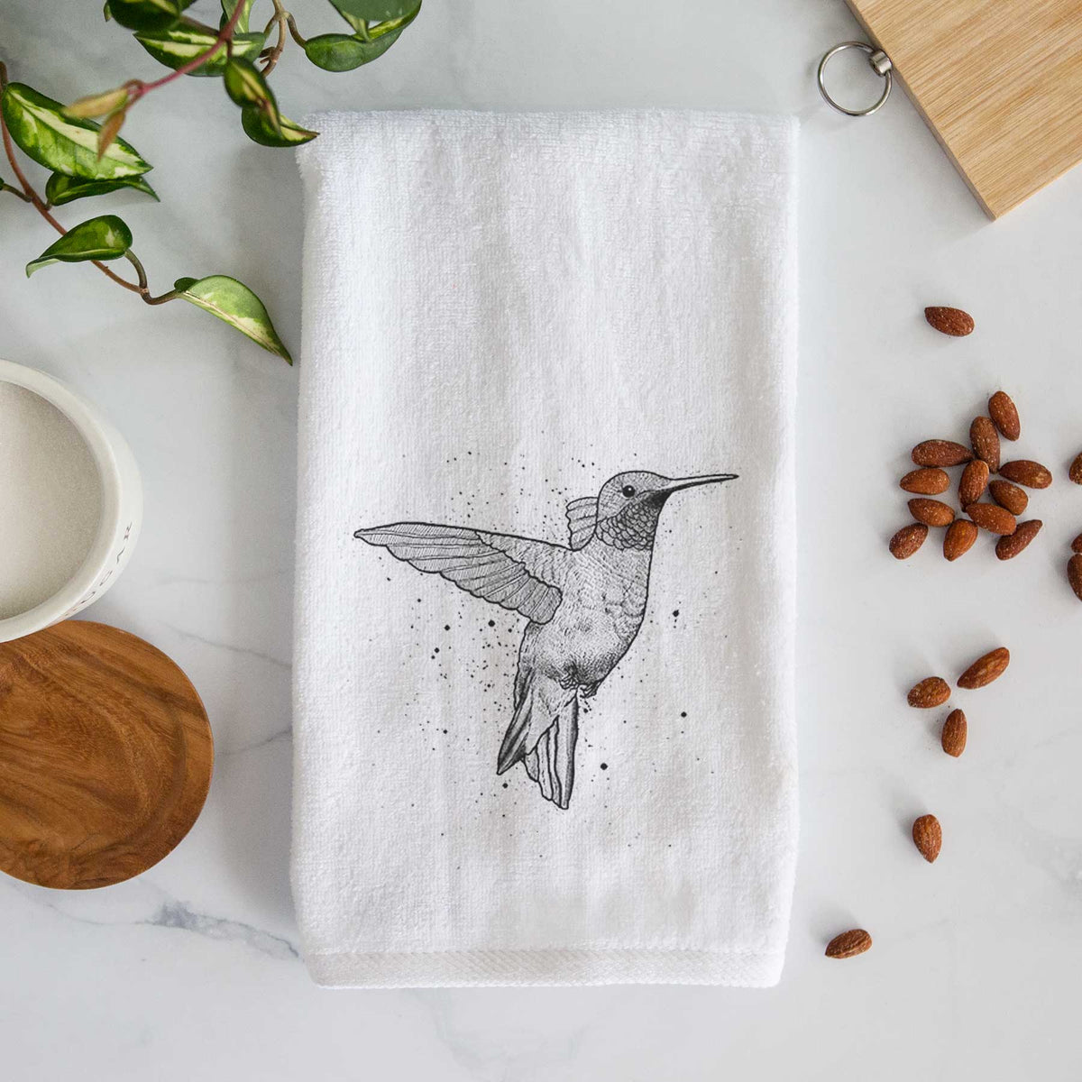 White hand towel printed with a black ink sketch of a ruby-throated hummingbird hovering with its wings raised.