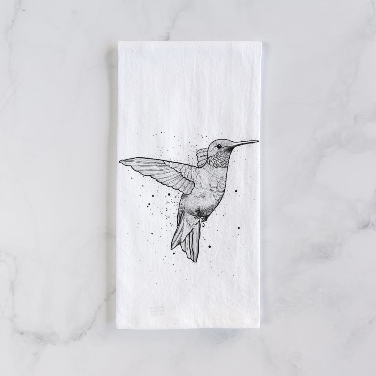 White cotton tea towel laid flat on marble, printed with a black ink sketch of a ruby-throated hummingbird hovering with its wings raised.