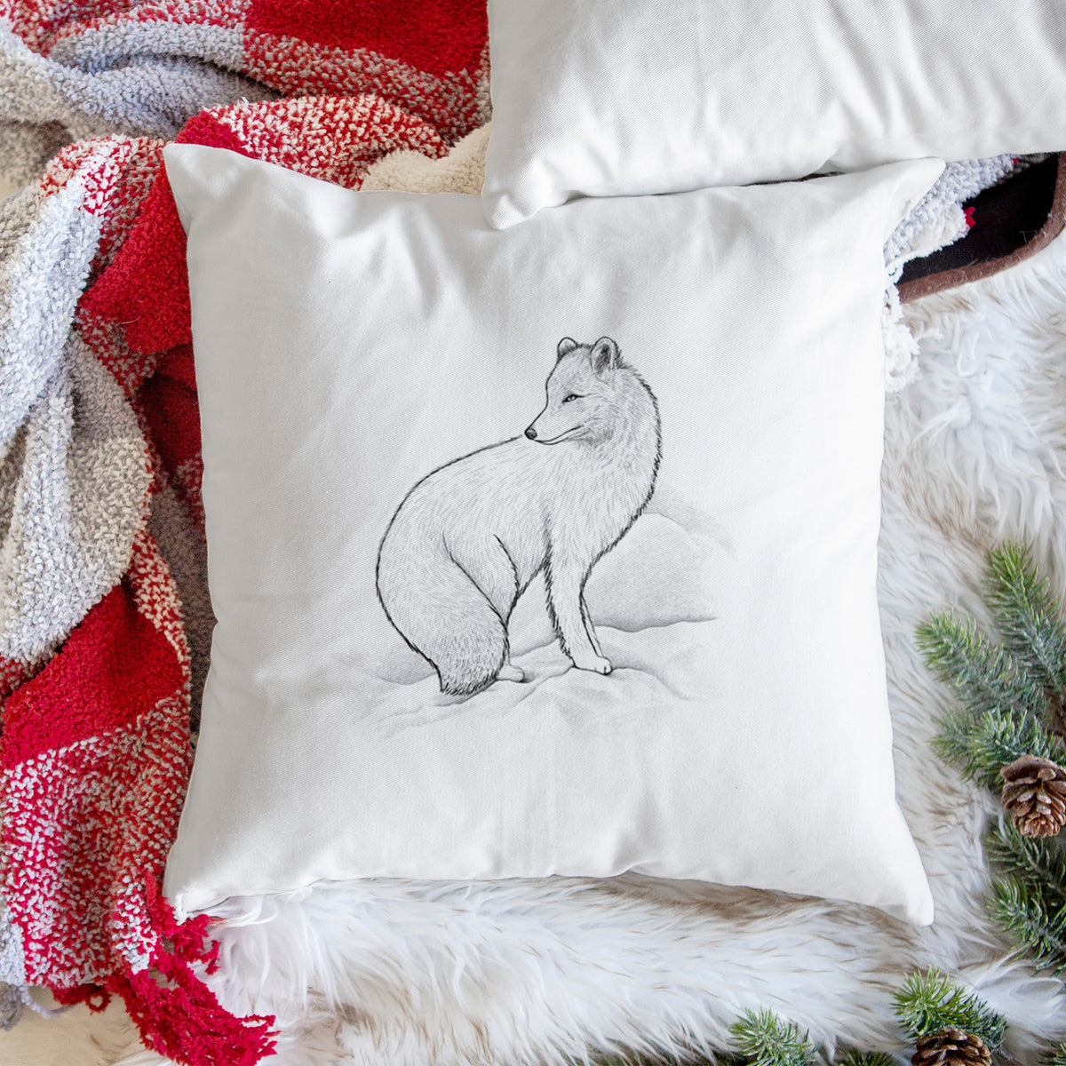 White pillow cover printed with a black ink illustration of an arctic fox sitting in the snow, on a woven chair.