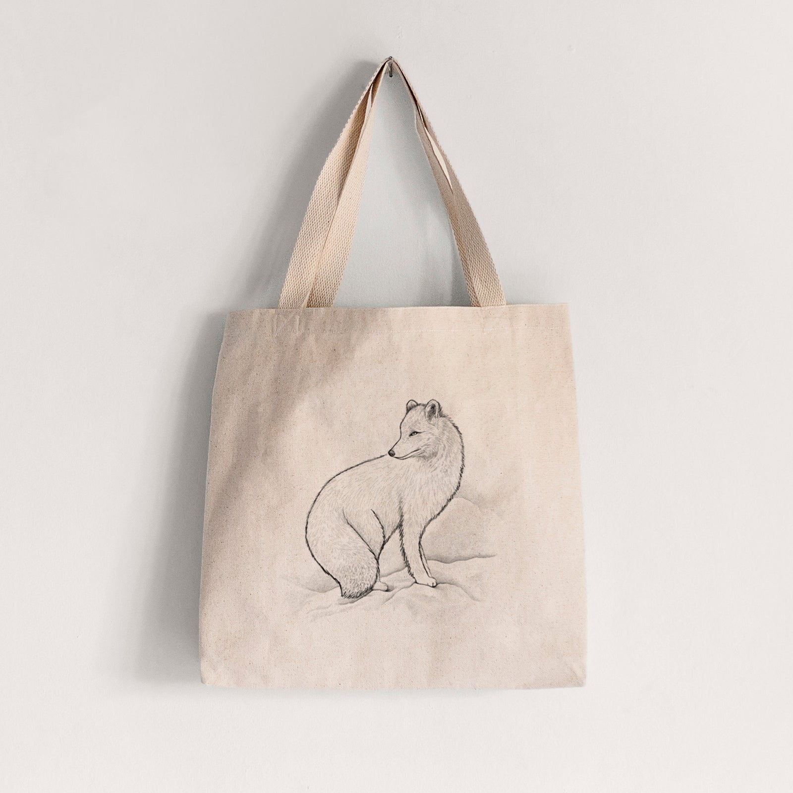 Natural canvas tote bag printed with a black ink illustration of an arctic fox sitting in the snow.