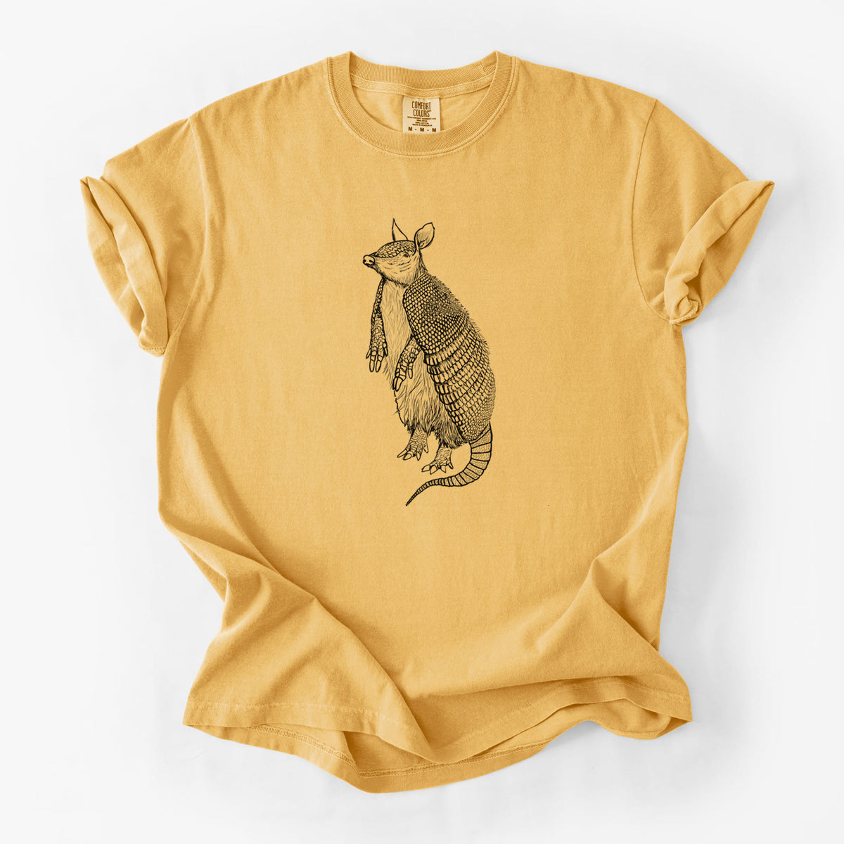Golden wheat yellow Comfort Colors t-shirt laid flat, printed with a black ink illustration of a nine-banded armadillo standing upright.