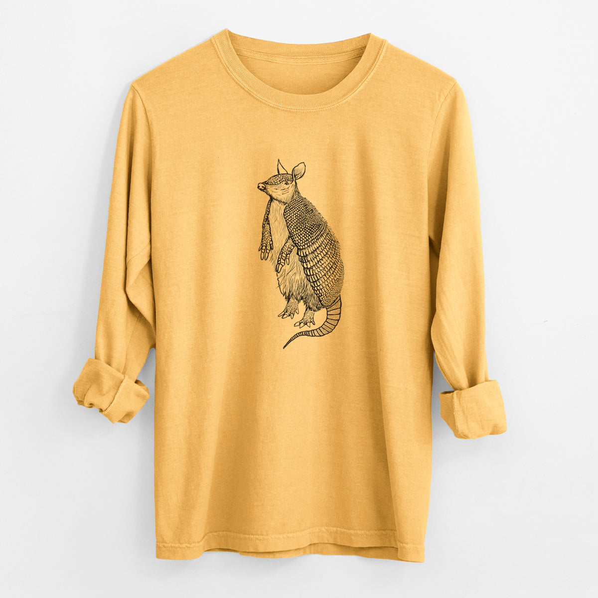 Golden wheat yellow Comfort Colors long sleeve shirt laid flat with the cuffs rolled, printed with a black ink illustration of a nine-banded armadillo standing upright.