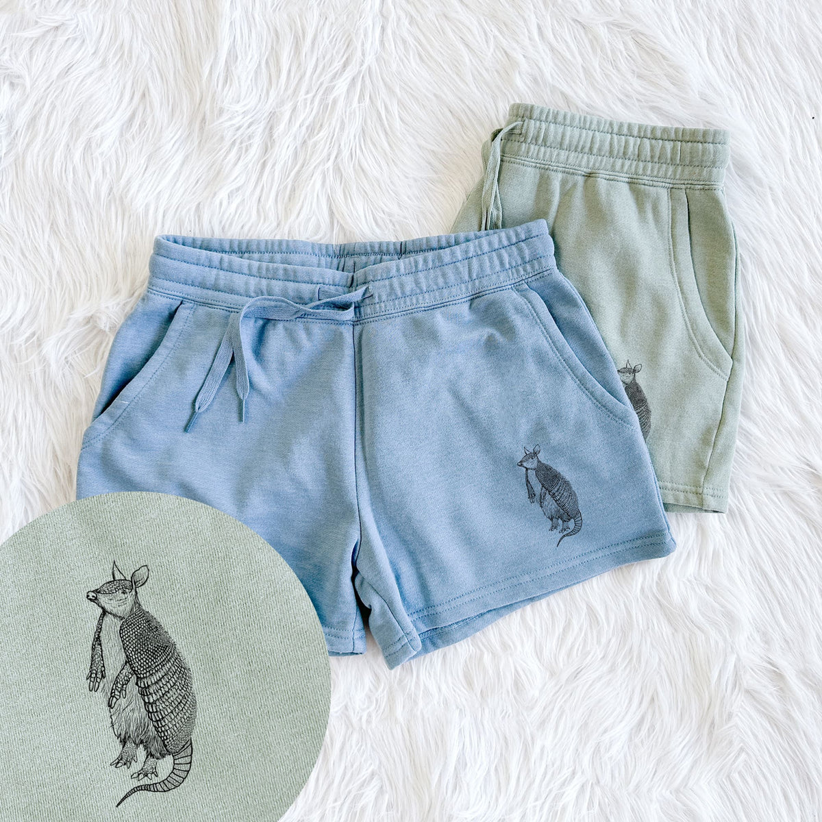 Two pairs of Cali Wave shorts in different colors printed with a black ink illustration of a nine-banded armadillo standing upright, with a close-up of the print.