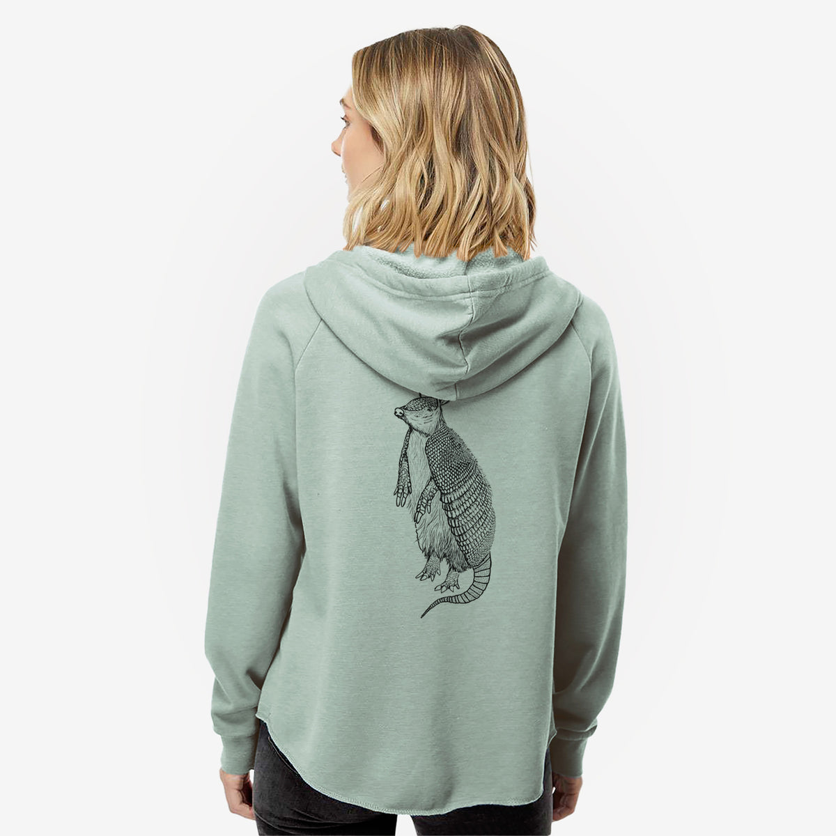 Woman wearing a sage green women's Cali Wave zip-up sweatshirt printed with a black ink illustration of a nine-banded armadillo standing upright, seen from behind.