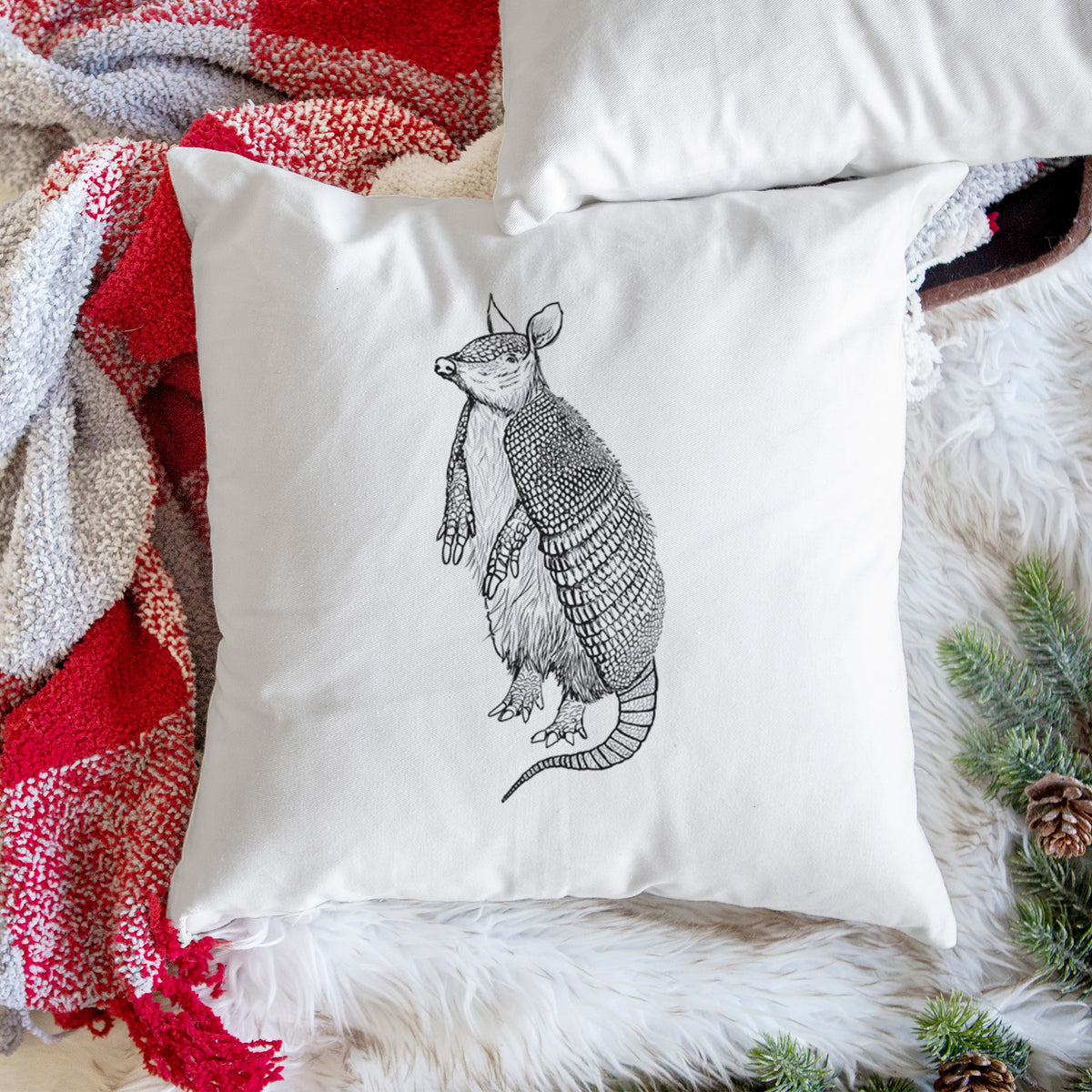 White pillow cover printed with a black ink illustration of a nine-banded armadillo standing upright, on a woven chair.
