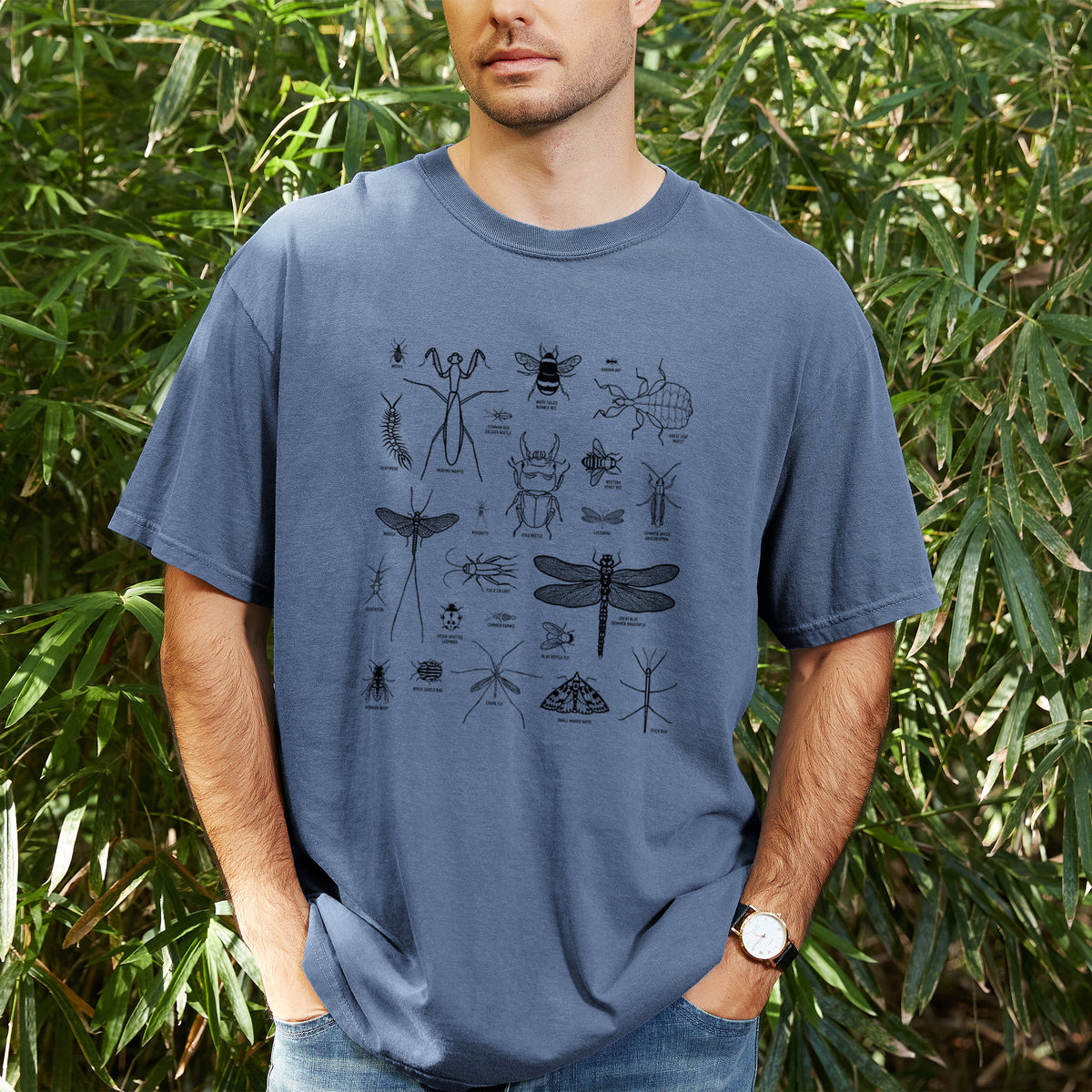 Man wearing a Comfort Colors t-shirt printed with a chart of black ink insect and arthropod illustrations, including dragonflies, beetles, spiders and bees, outdoors.
