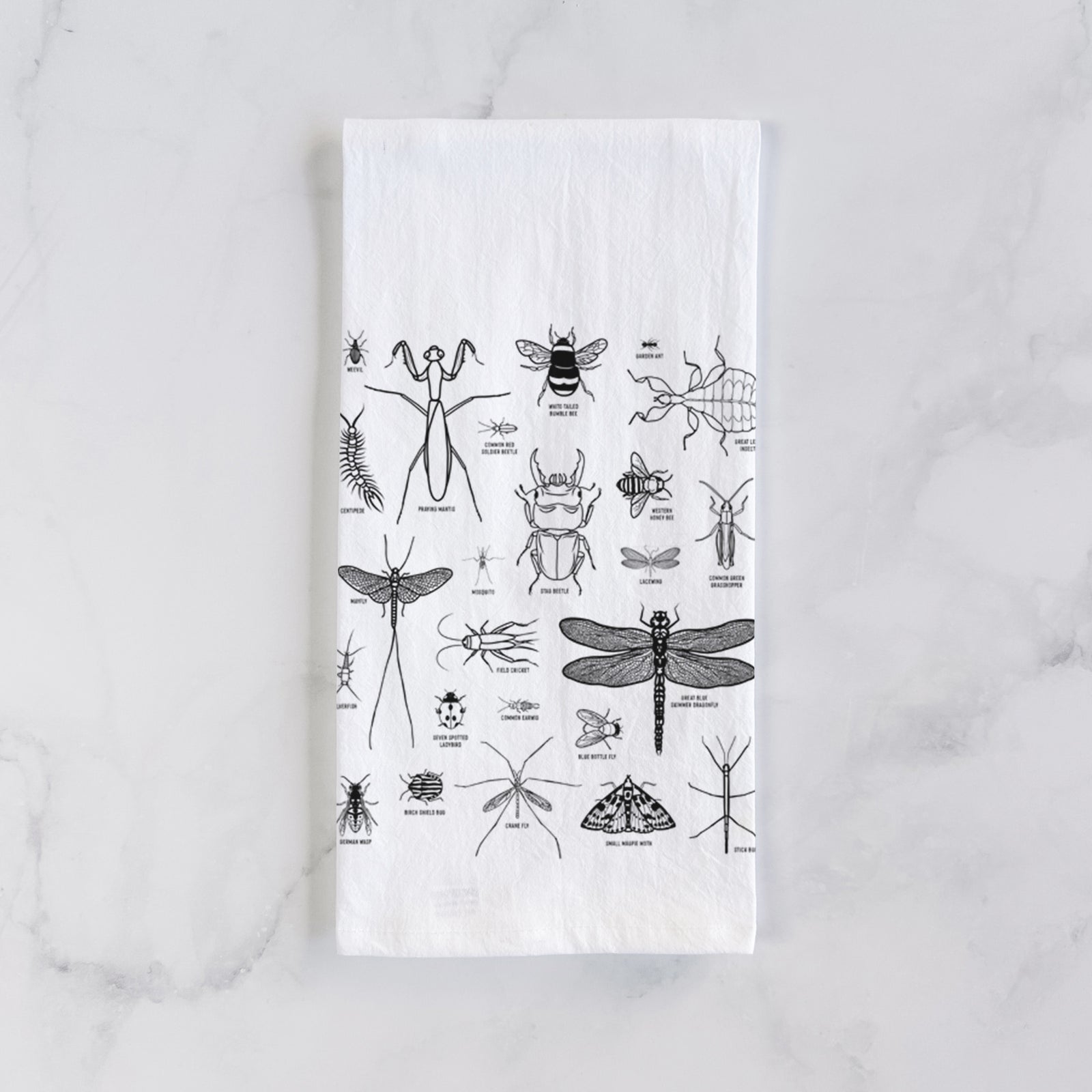 White cotton tea towel printed with a chart of black ink insect and arthropod illustrations, including dragonflies, beetles, spiders and bees, on a marble counter beside a round wooden cutting board and greenery.