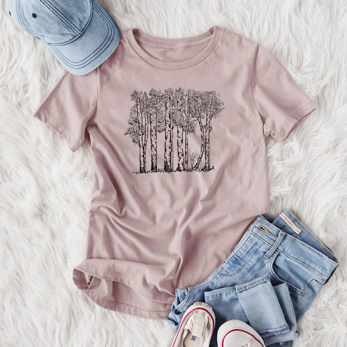 Women's relaxed fit cotton t-shirt printed with a black ink illustration of a grove of aspen trees, styled flat on a white faux fur rug with jeans.