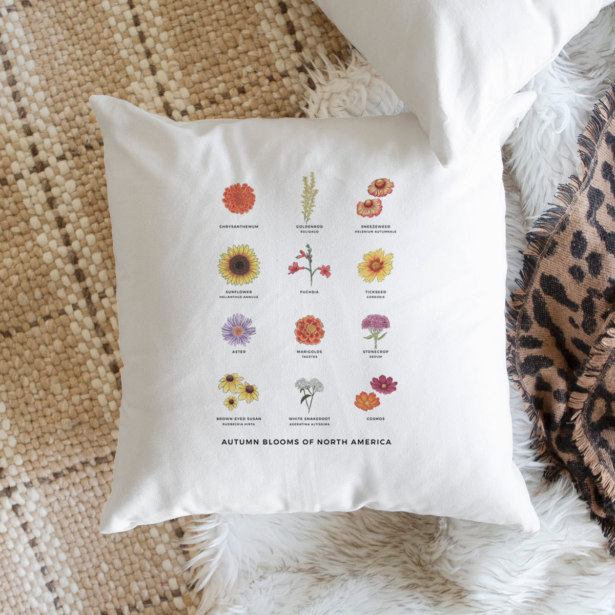 White pillow cover printed with a full-color chart of autumn flowers, each labeled with its name, on a woven chair.