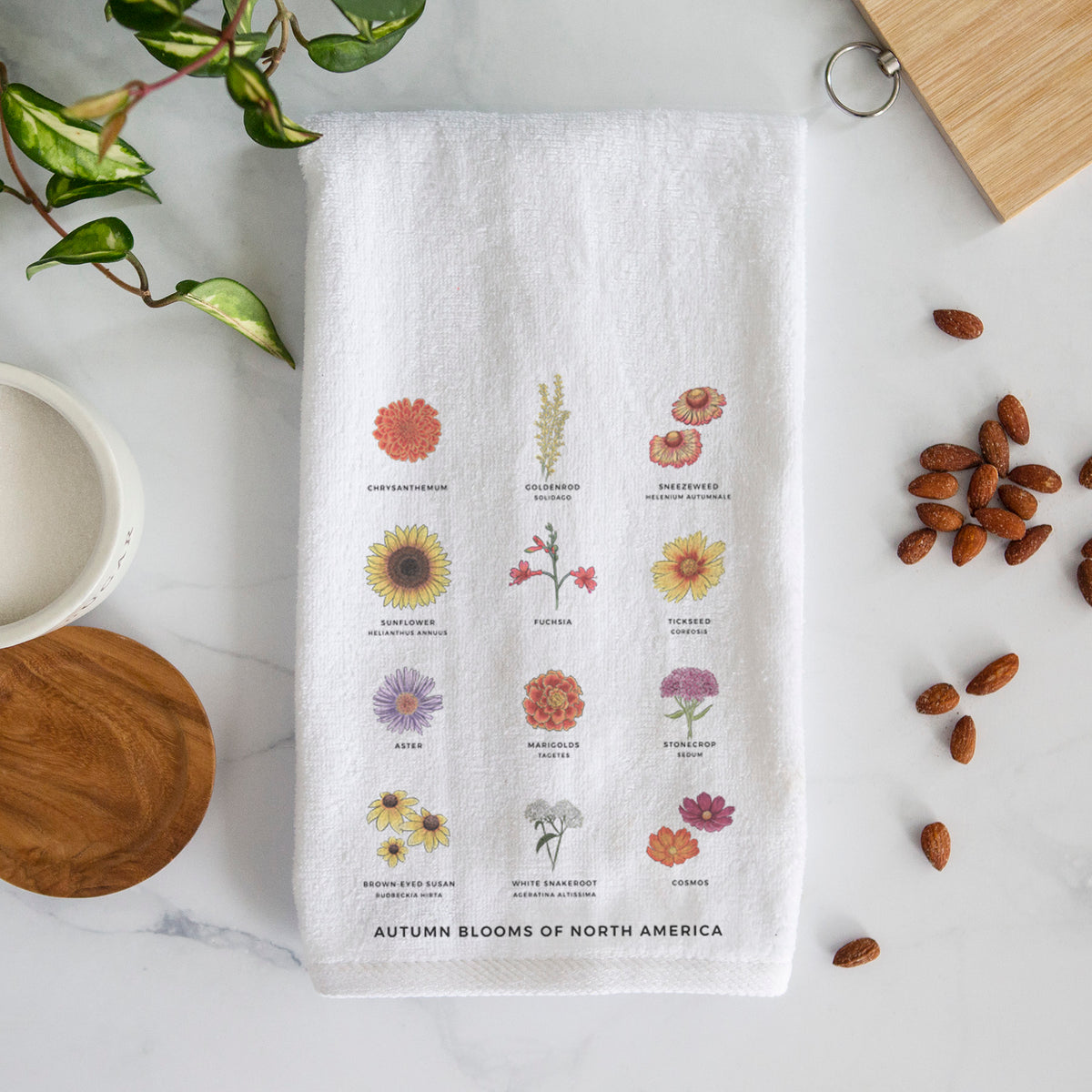 White hand towel printed with a full-color chart of autumn flowers, each labeled with its name.