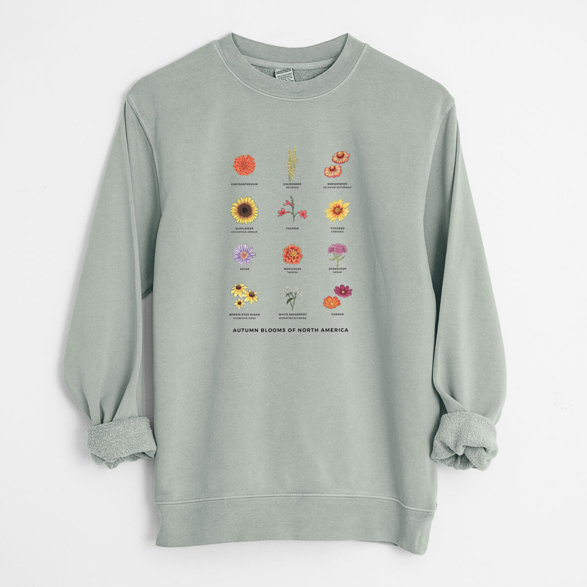 Sage green pigment dyed crewneck sweatshirt laid flat with the sleeves rolled, printed with a full-color chart of autumn flowers, each labeled with its name.