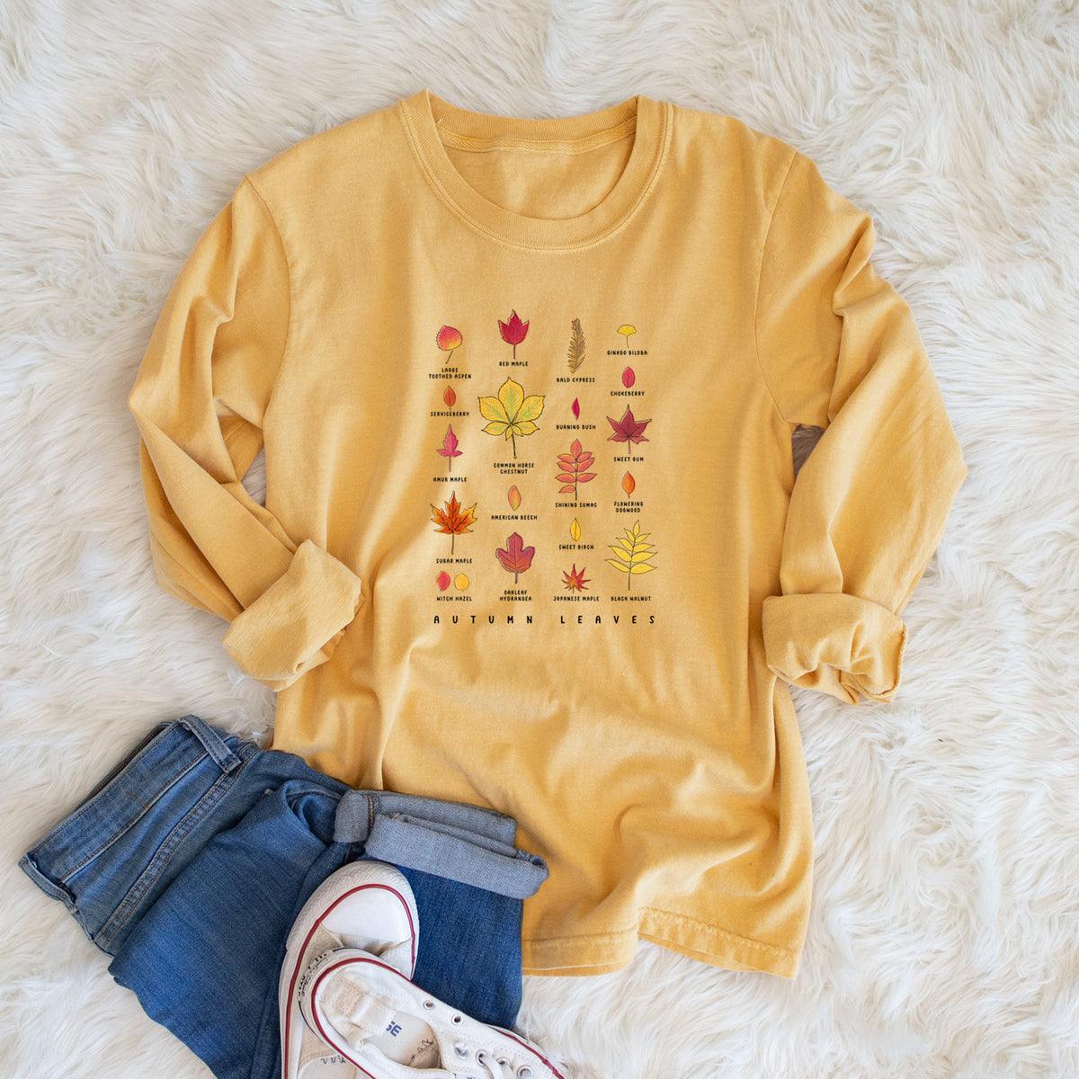 Golden wheat yellow Comfort Colors long sleeve shirt printed with a full-color chart of autumn leaves, each labeled with its tree species, shown in a lifestyle photo.