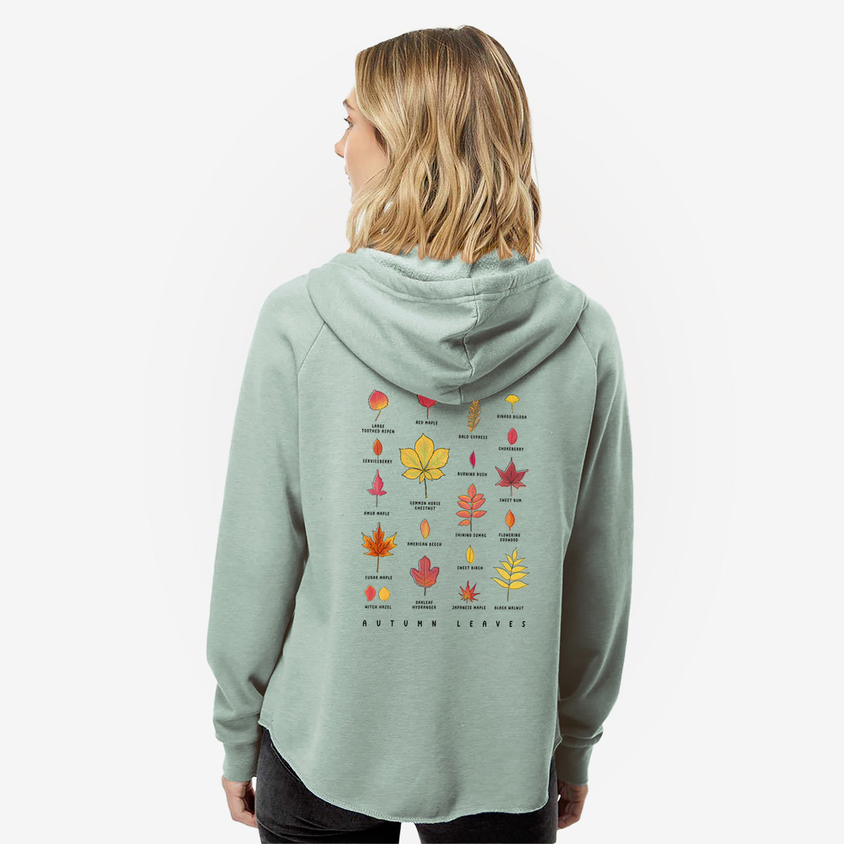 Woman wearing a sage green women's Cali Wave zip-up sweatshirt printed with a full-color chart of autumn leaves, each labeled with its tree species, seen from behind.