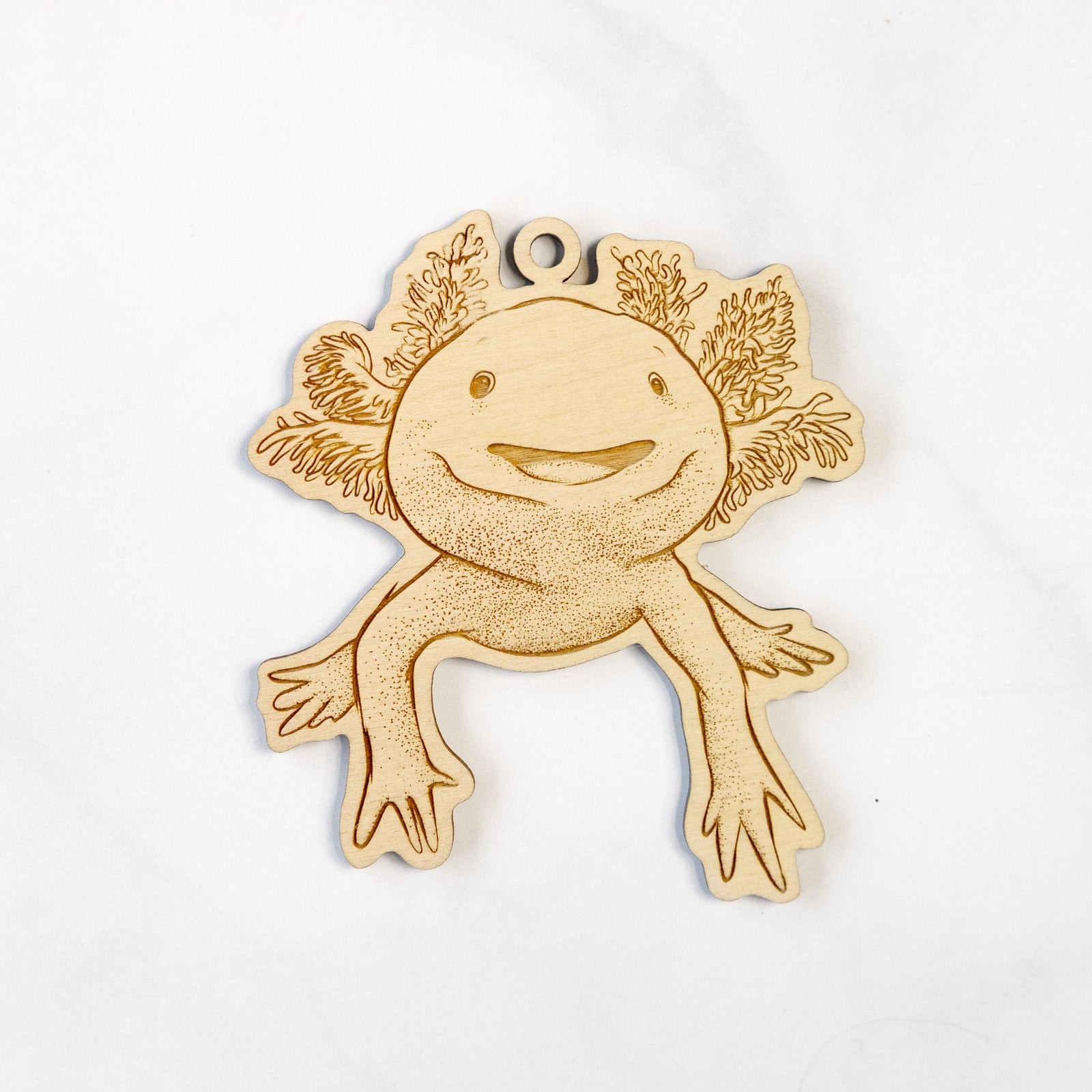 Wooden ornament featuring a engraving of a smiling axolotl with feathery gills, hanging on a Christmas tree.