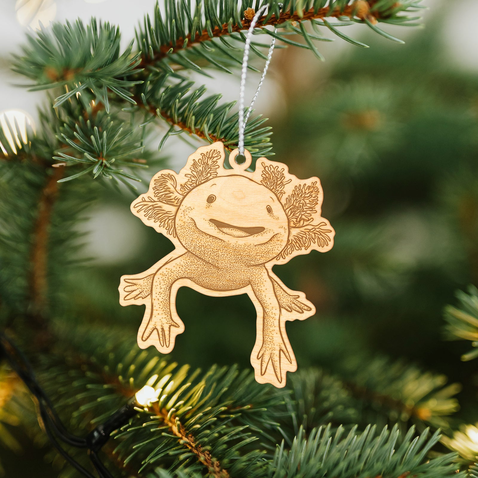 Wooden ornament featuring a engraving of a smiling axolotl with feathery gills, hanging on a Christmas tree.