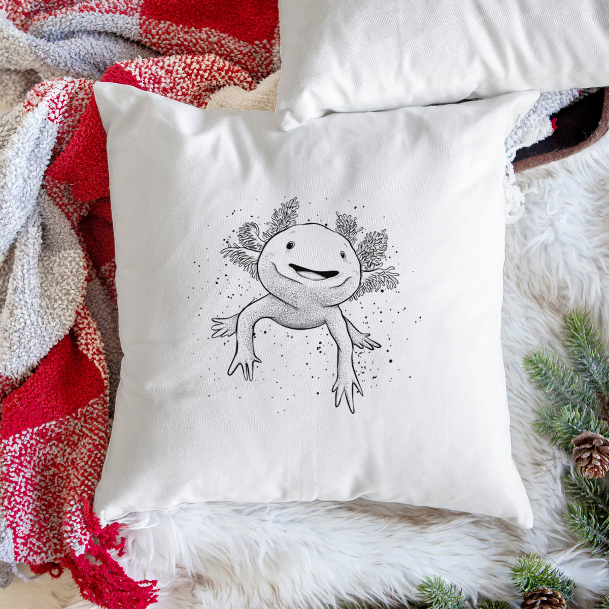 White pillow cover printed with a black ink illustration of a smiling axolotl with feathery gills, on a woven chair.