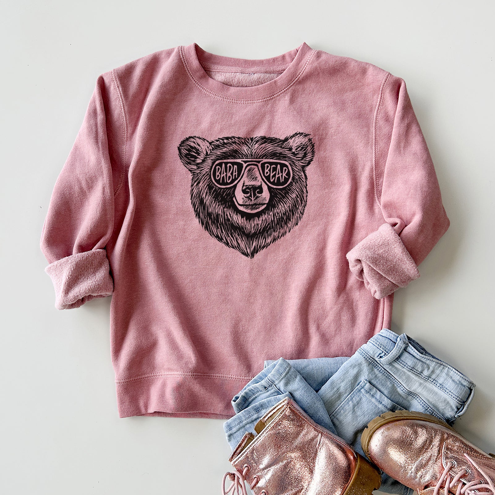 Boy wearing a youth crewneck sweatshirt printed with a black ink bear's face wearing sunglasses that read Baba Bear, outdoors.