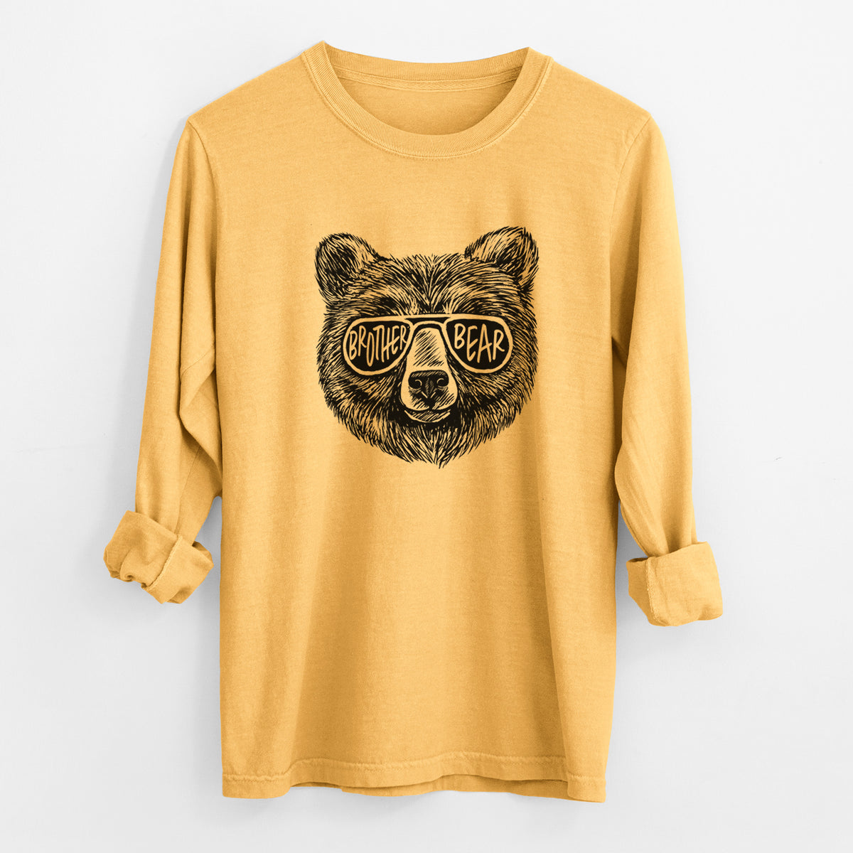 Golden wheat yellow Comfort Colors long sleeve shirt laid flat with the cuffs rolled, printed with a black ink bear's face wearing sunglasses that read Brother Bear.