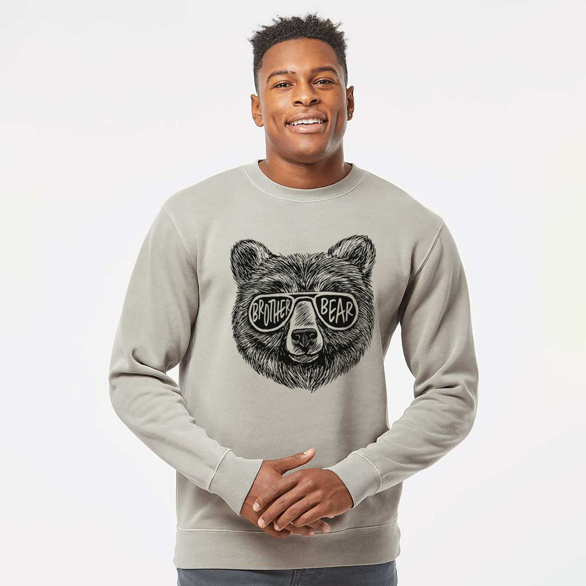 Model wearing a cement grey pigment dyed crewneck sweatshirt printed with a black ink bear's face wearing sunglasses that read Brother Bear.