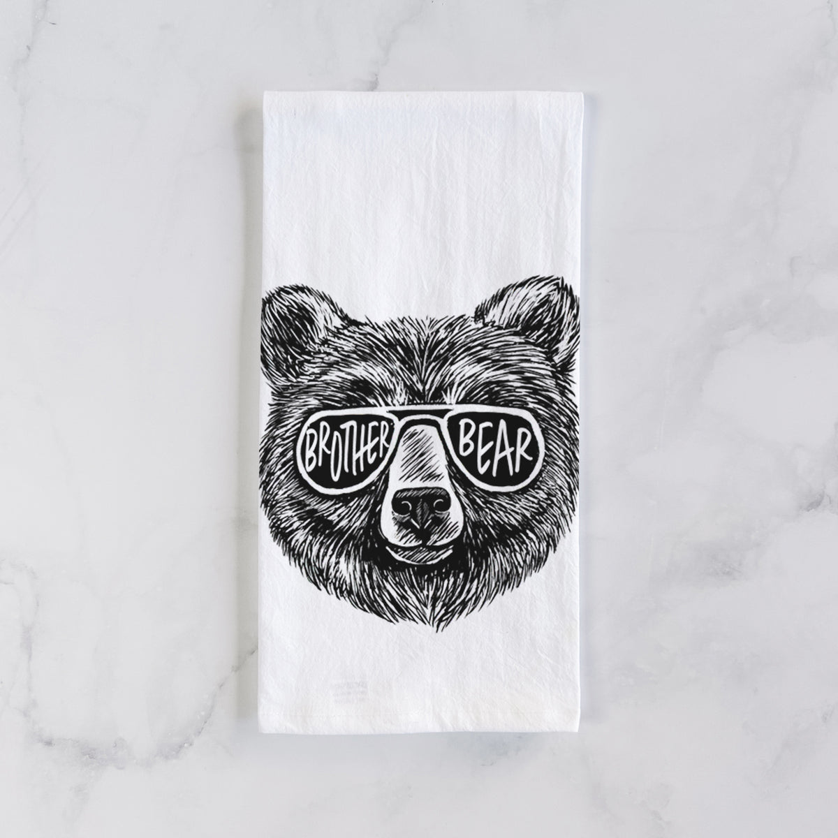 White cotton tea towel laid flat on marble, printed with a black ink bear's face wearing sunglasses that read Brother Bear.