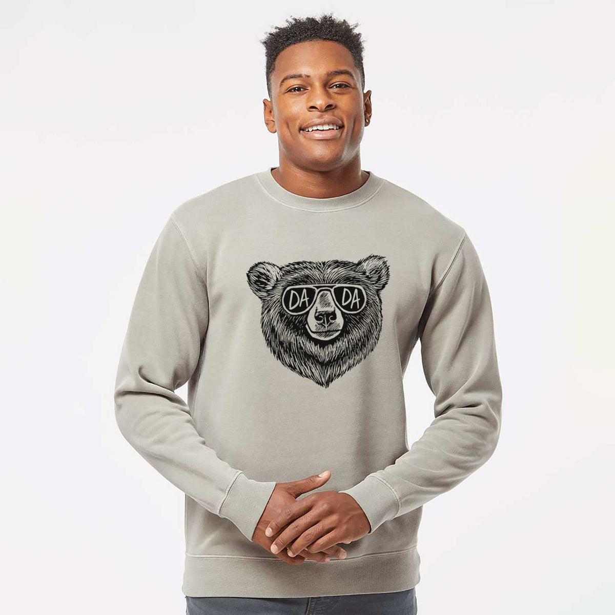 Model wearing a cement grey pigment dyed crewneck sweatshirt printed with a black ink bear's face wearing sunglasses that read Dada.
