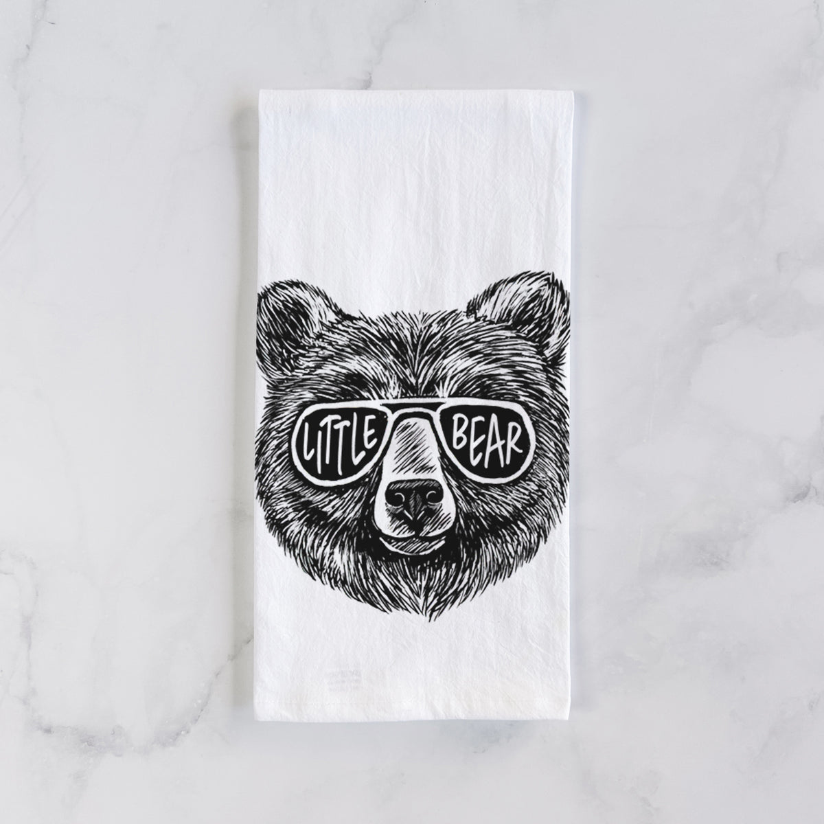 White cotton tea towel laid flat on marble, printed with a black ink bear's face wearing sunglasses that read Little Bear.