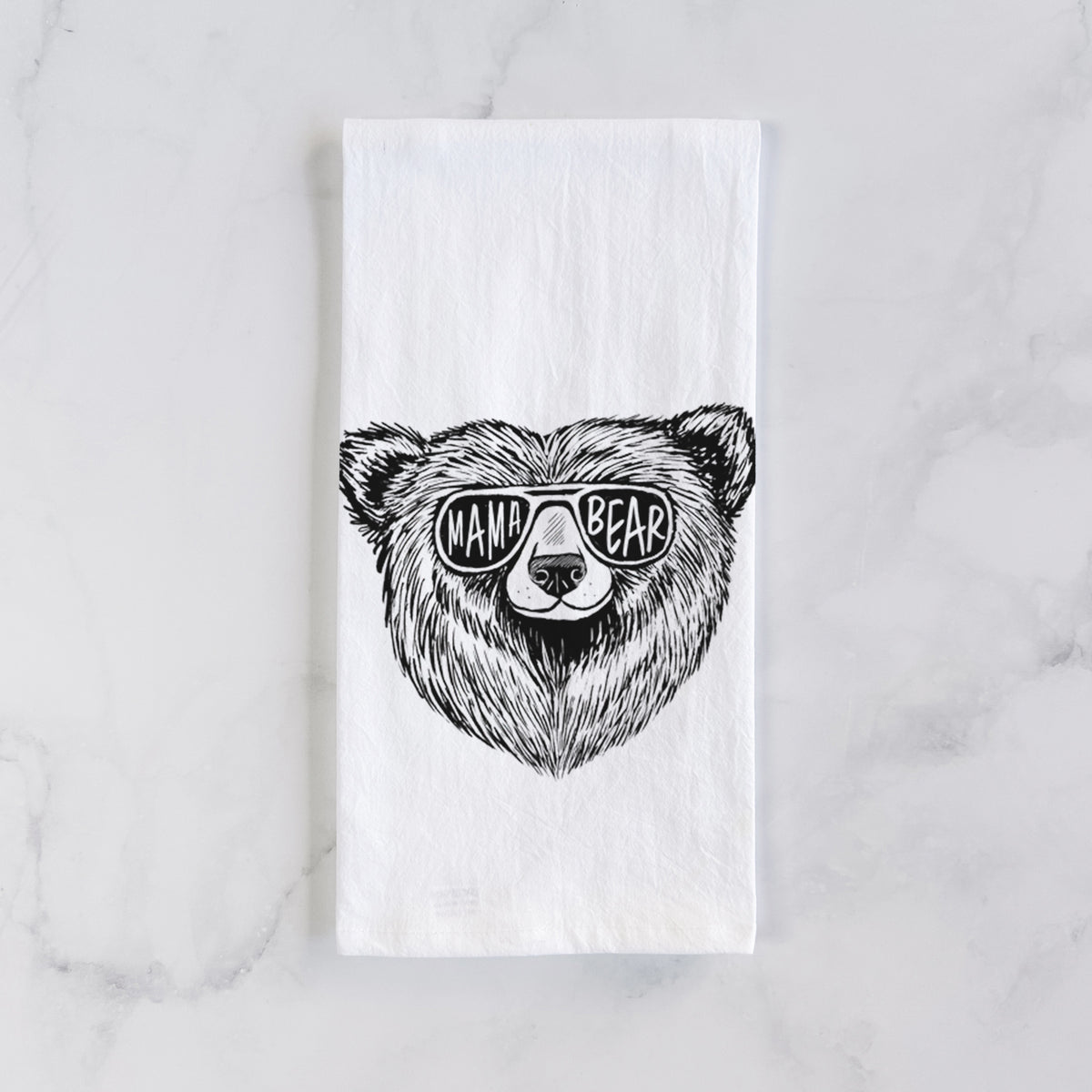 White cotton tea towel laid flat on marble, printed with a black ink bear's face wearing sunglasses that read Mama Bear.