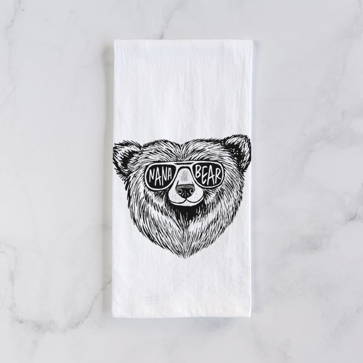 White cotton tea towel laid flat on marble, printed with a black ink bear's face wearing sunglasses that read Nana Bear.