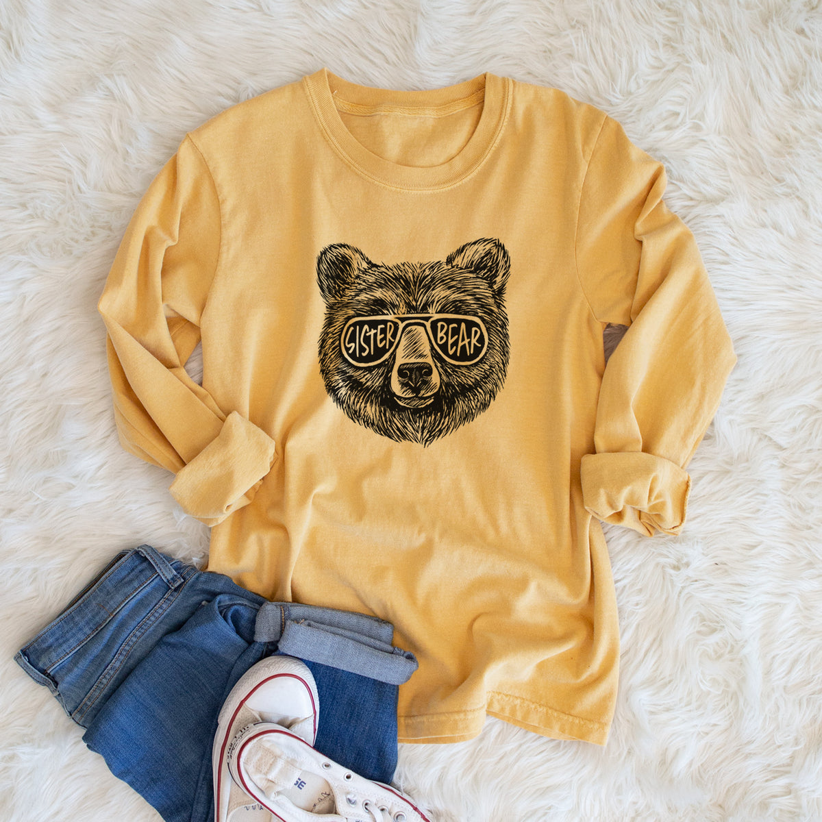 Golden wheat yellow Comfort Colors long sleeve shirt printed with a black ink bear's face wearing sunglasses that read Sister Bear, shown in a lifestyle photo.