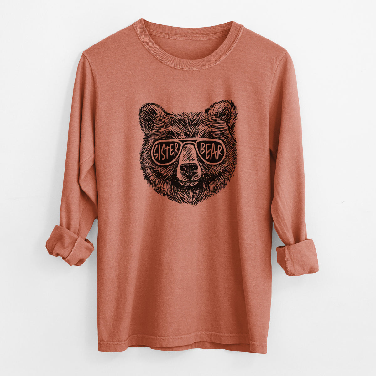 Yam burnt orange Comfort Colors long sleeve shirt laid flat with the cuffs rolled, printed with a black ink bear's face wearing sunglasses that read Sister Bear.