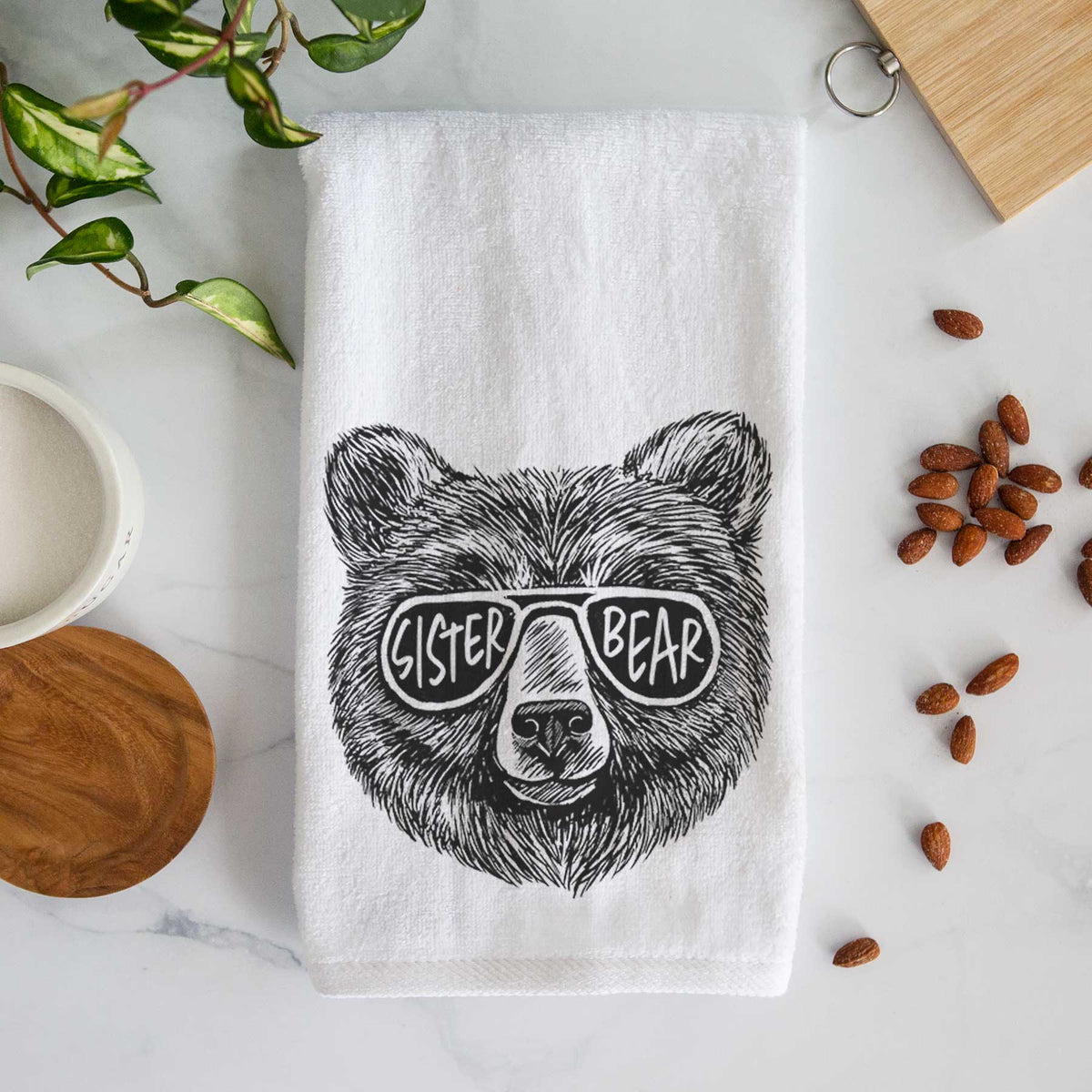 White hand towel printed with a black ink bear's face wearing sunglasses that read Sister Bear.