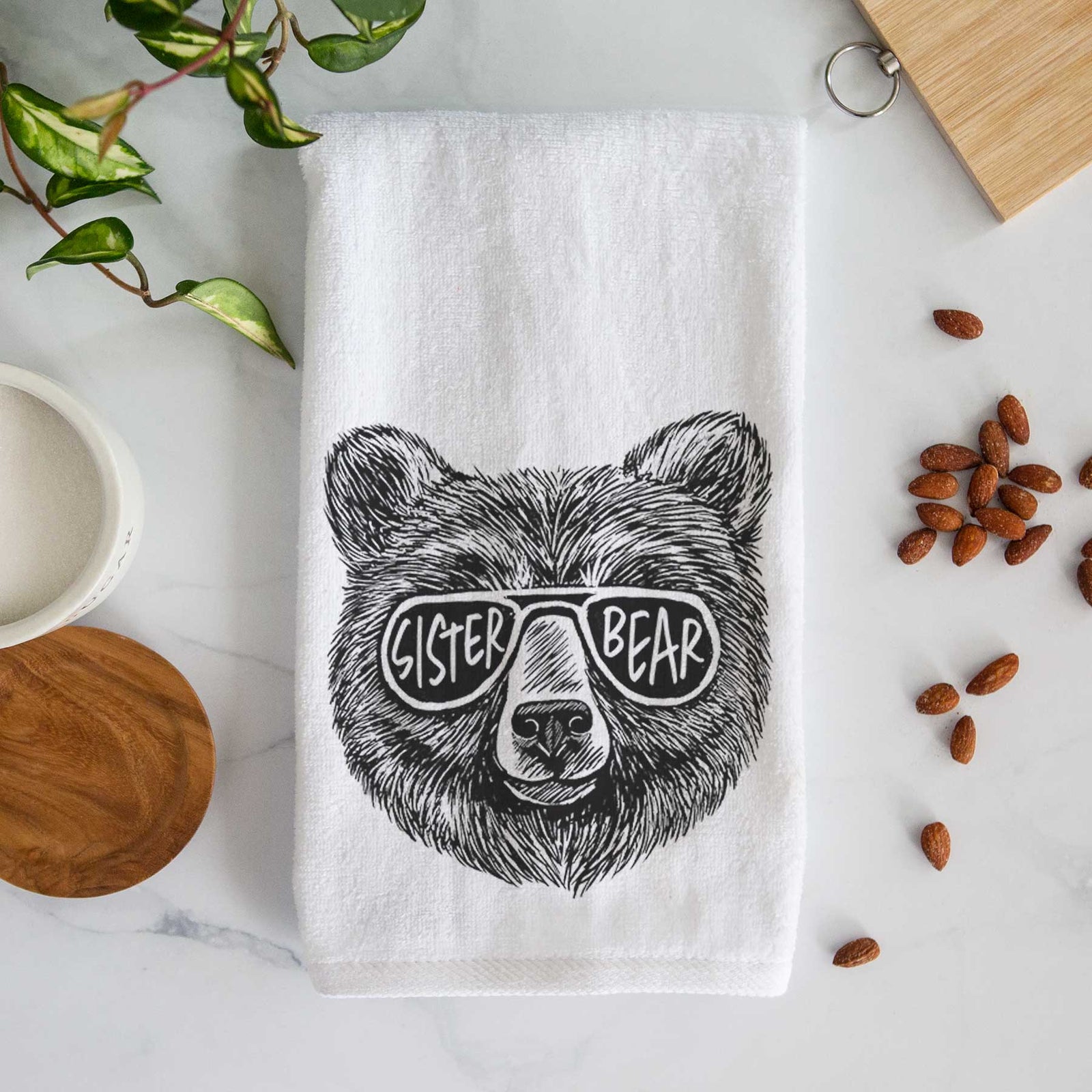 White hand towel printed with a black ink bear's face wearing sunglasses that read Sister Bear.