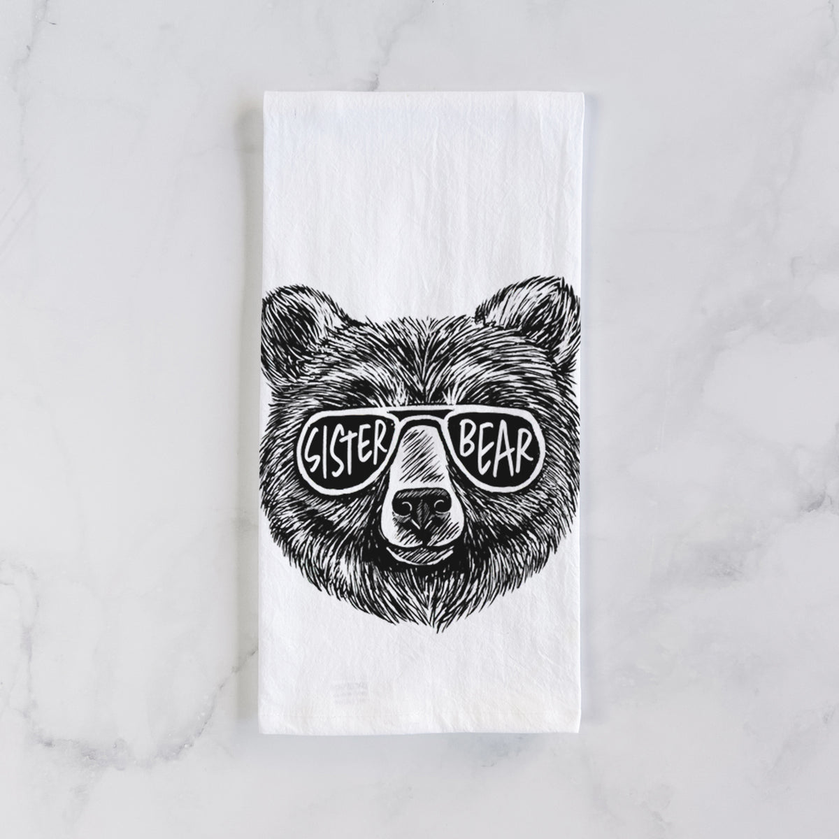 White cotton tea towel laid flat on marble, printed with a black ink bear's face wearing sunglasses that read Sister Bear.