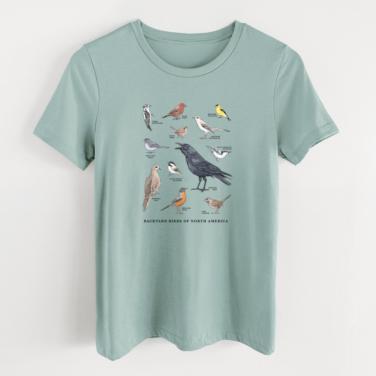 Dusty blue women's relaxed fit cotton t-shirt laid flat, printed with a full-color chart of North American backyard birds, each labeled with its species.