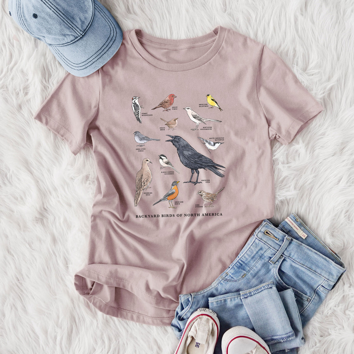 Women's relaxed fit cotton t-shirt printed with a full-color chart of North American backyard birds, each labeled with its species, styled flat on a white faux fur rug with jeans.