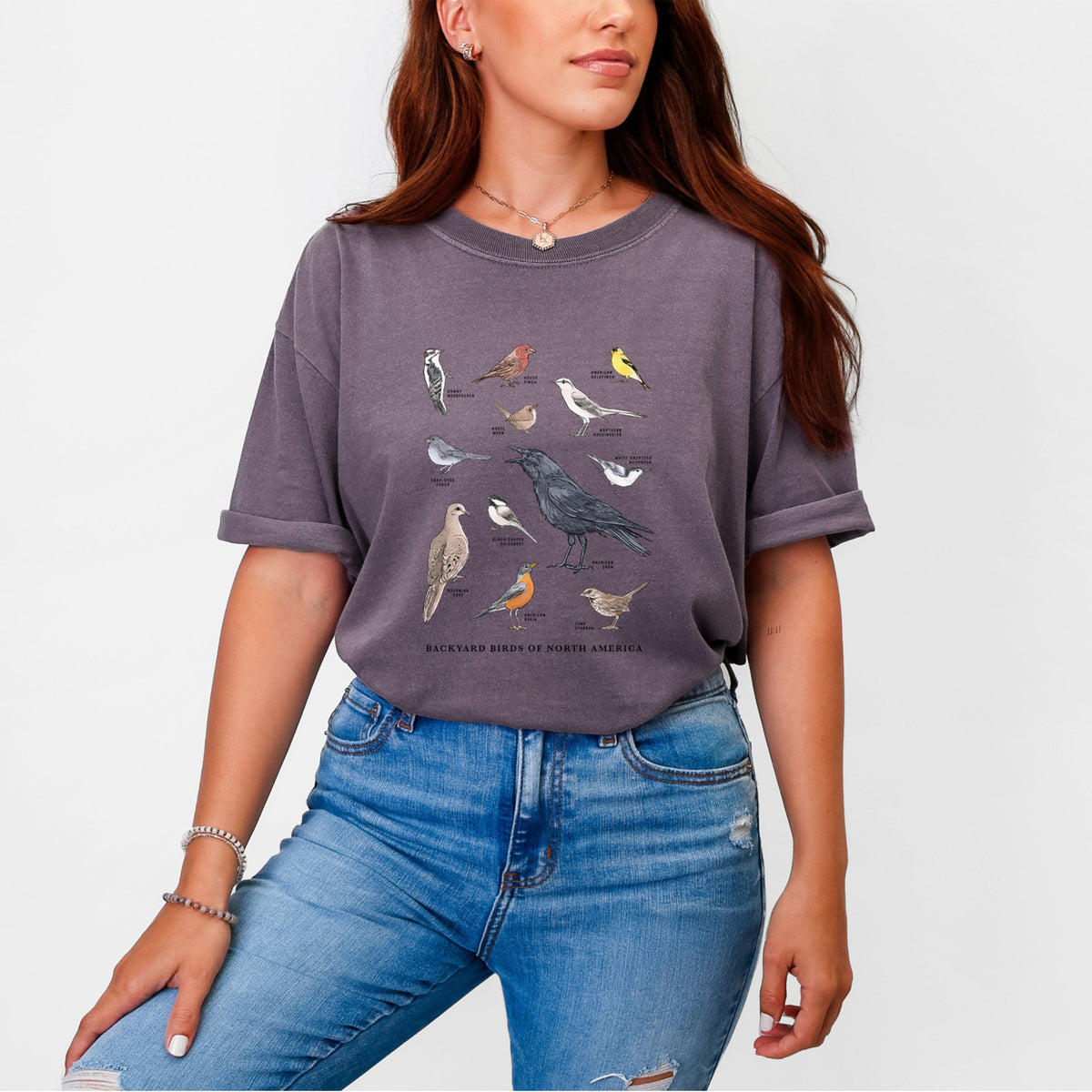 Woman wearing a Comfort Colors t-shirt printed with a full-color chart of North American backyard birds, each labeled with its species.