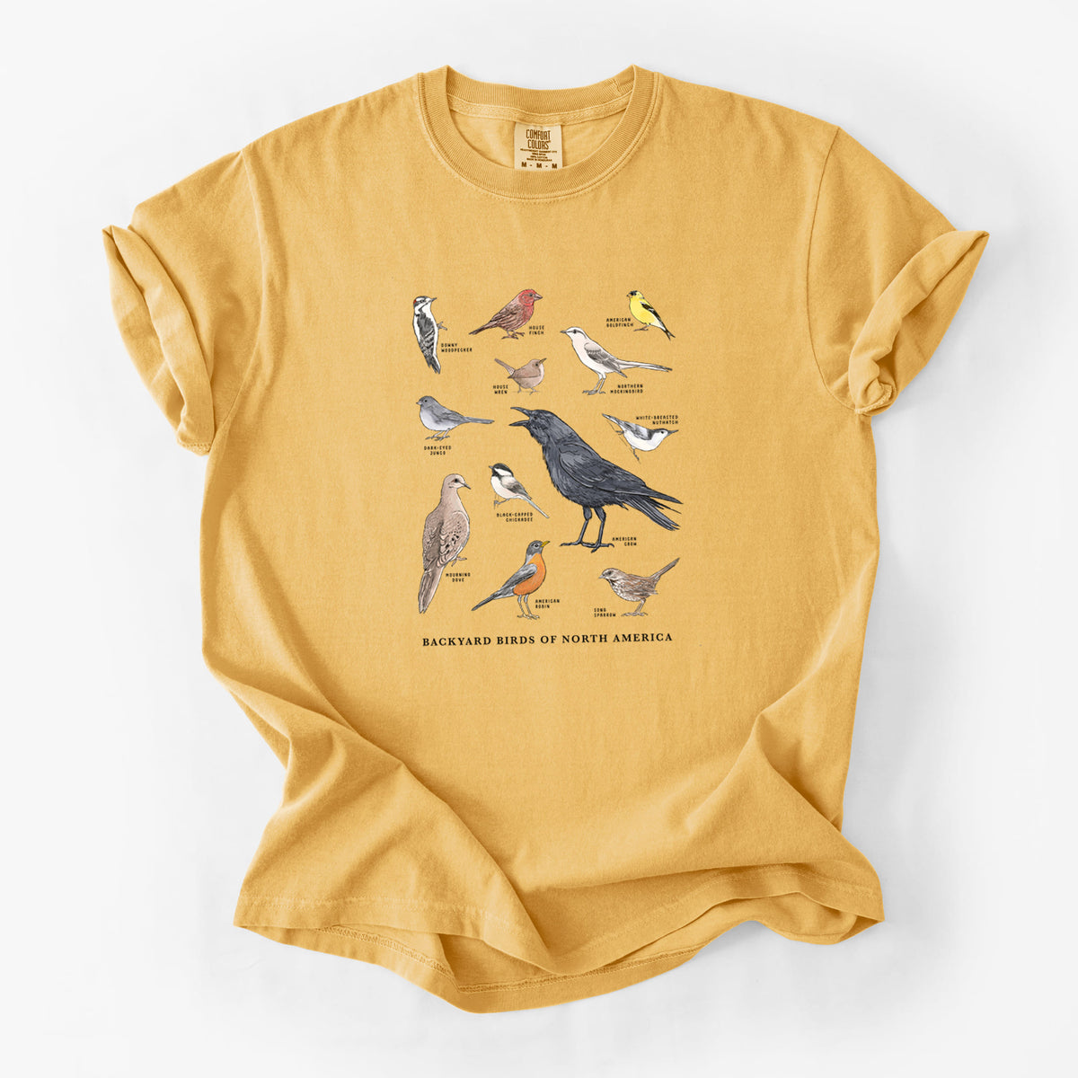 Golden wheat yellow Comfort Colors t-shirt laid flat, printed with a full-color chart of North American backyard birds, each labeled with its species.