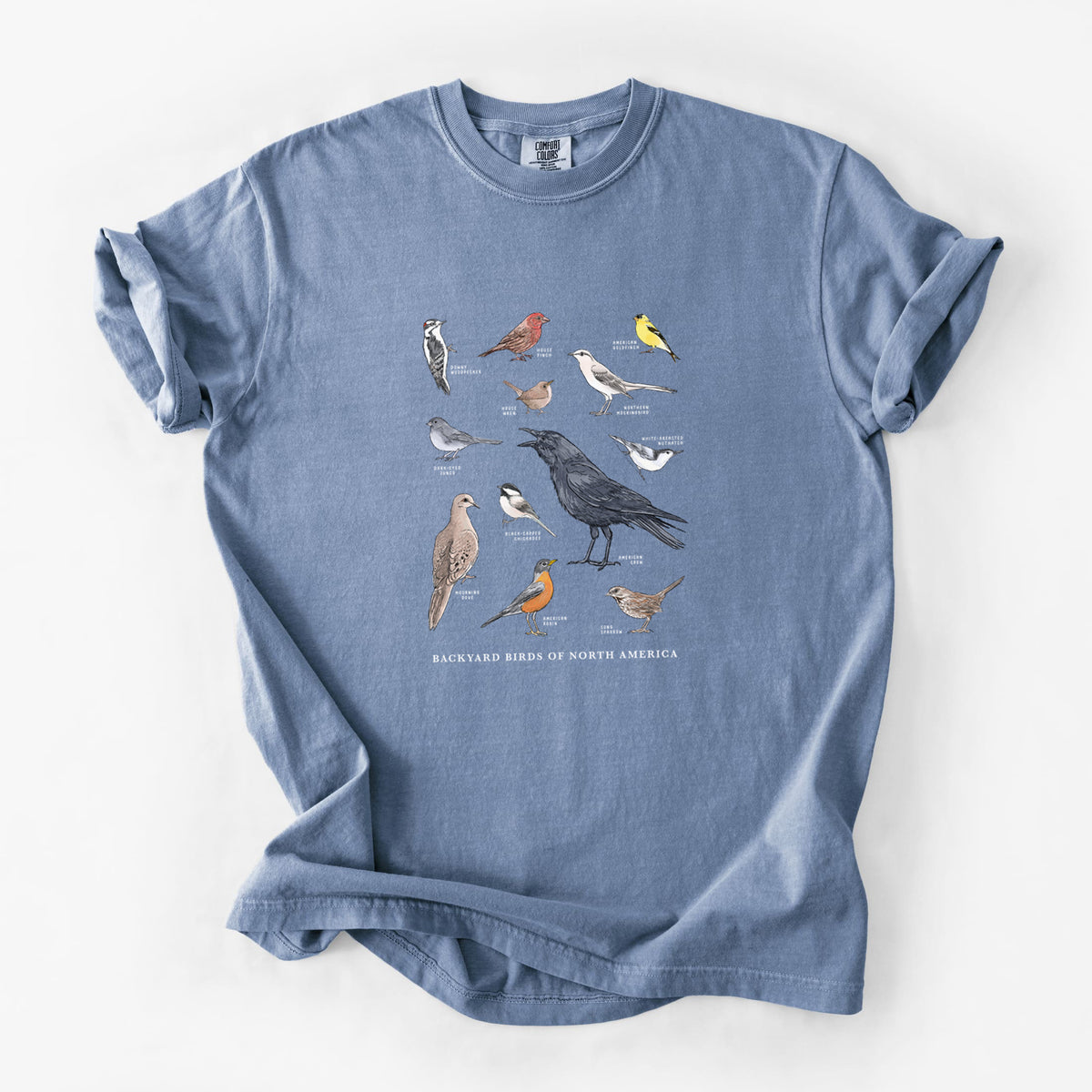 Blue jean Comfort Colors t-shirt laid flat, printed with a full-color chart of North American backyard birds, each labeled with its species.