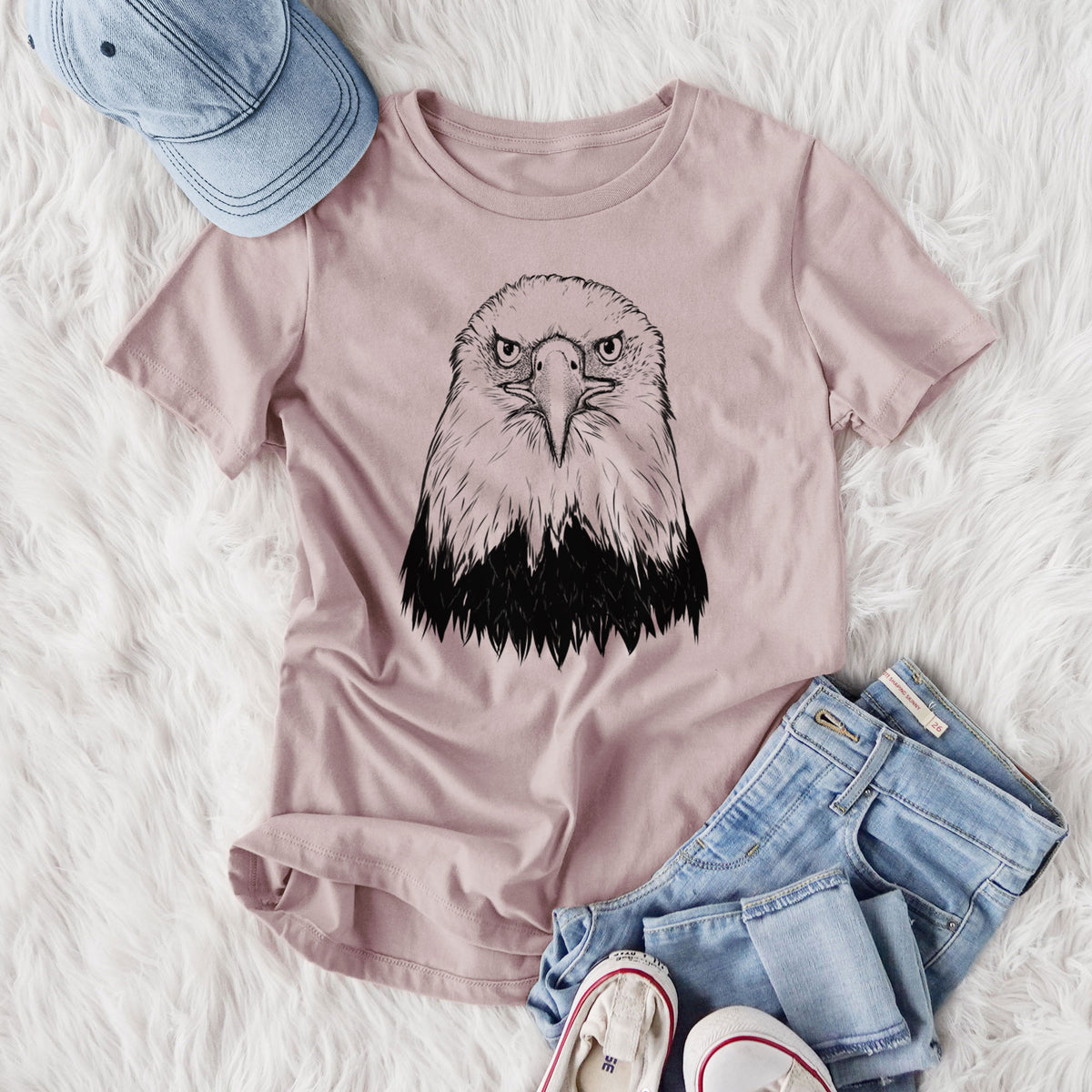 Women's relaxed fit cotton t-shirt printed with a detailed black ink portrait of a bald eagle facing forward, styled flat on a white faux fur rug with jeans.