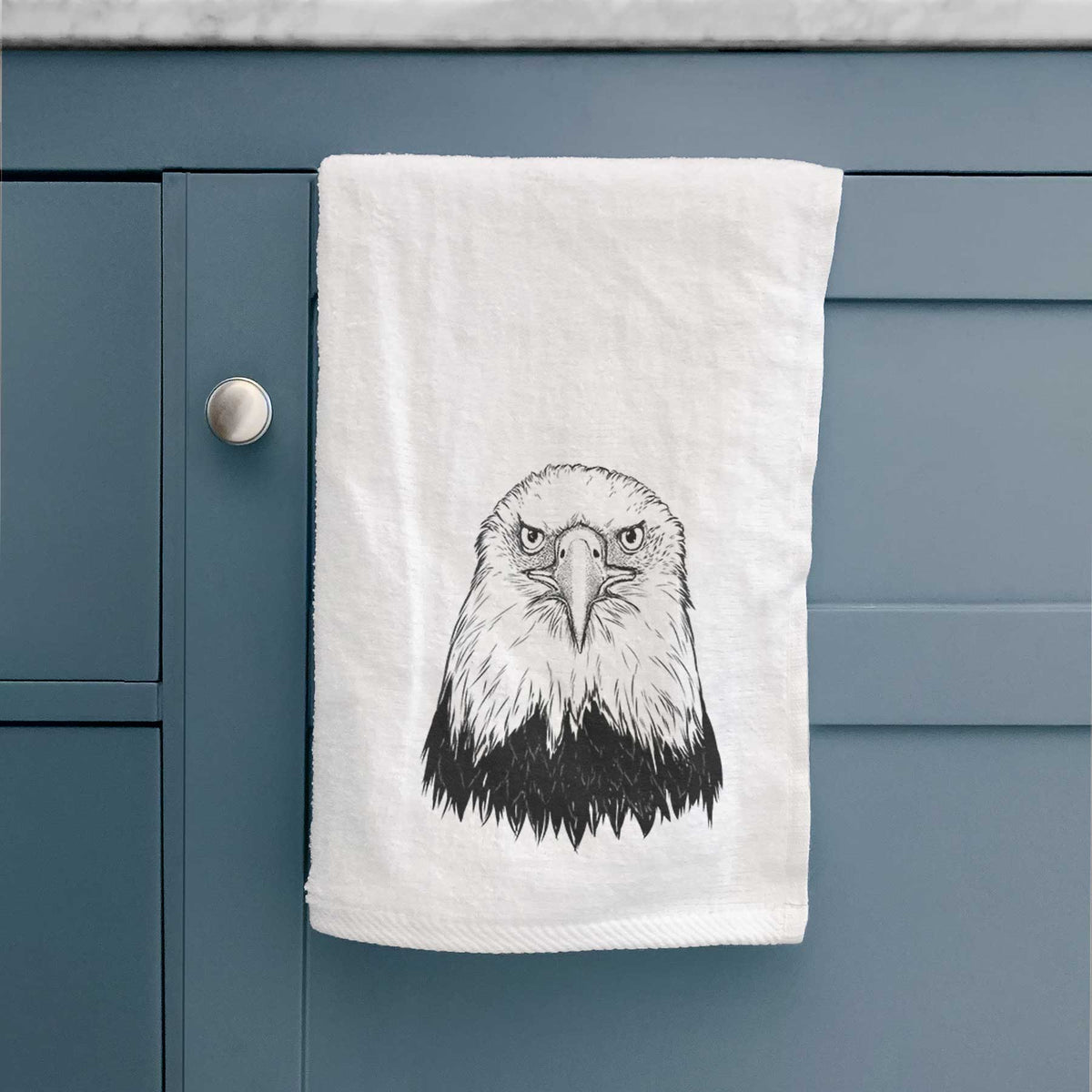 White hand towel printed with a detailed black ink portrait of a bald eagle facing forward, hanging on a cabinet door.