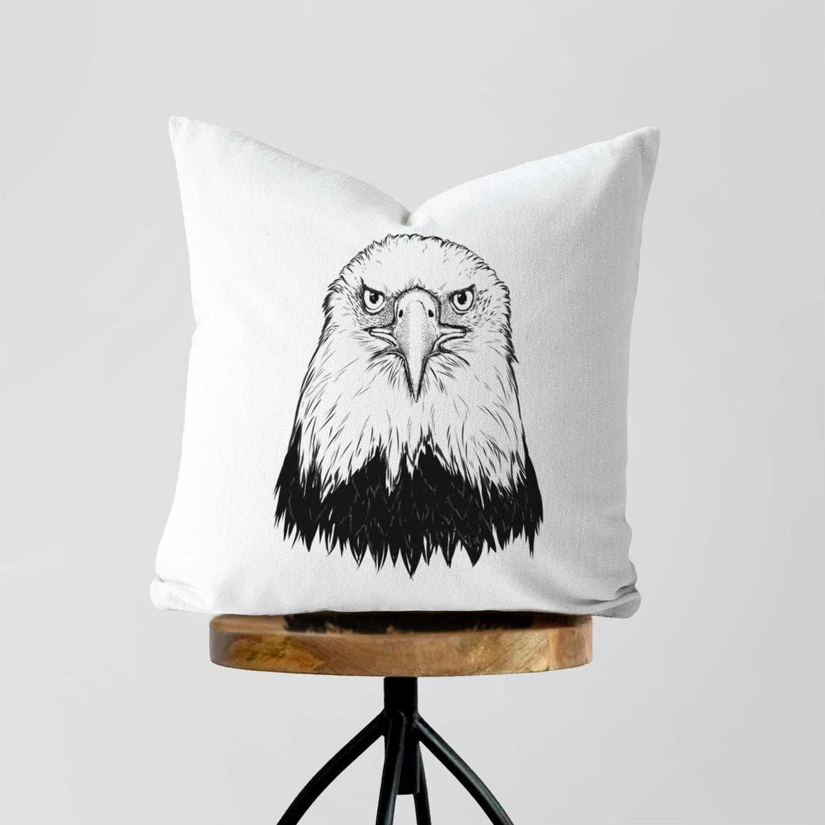 White pillow cover printed with a detailed black ink portrait of a bald eagle facing forward, on a wooden stool.