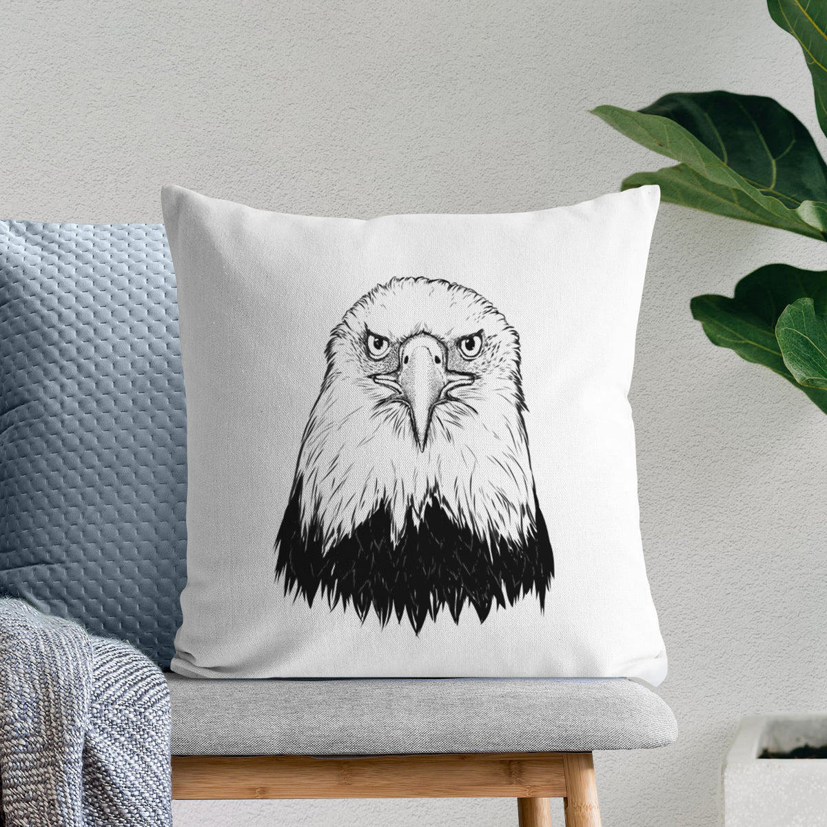 White pillow cover printed with a detailed black ink portrait of a bald eagle facing forward, on a bench beside plants.