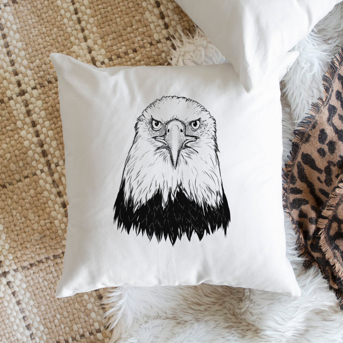 White pillow cover printed with a detailed black ink portrait of a bald eagle facing forward, on a woven chair.