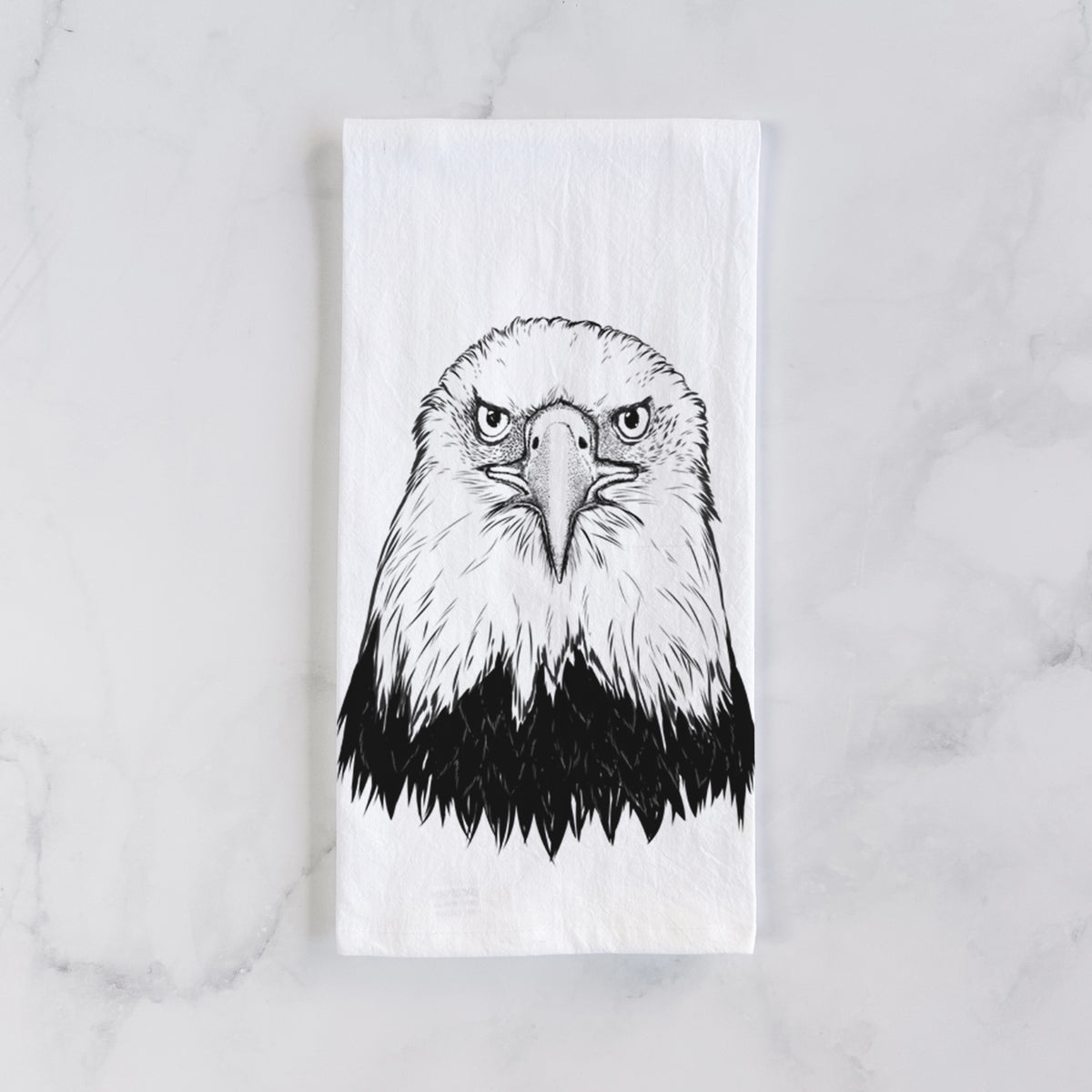 White cotton tea towel laid flat on marble, printed with a detailed black ink portrait of a bald eagle facing forward.