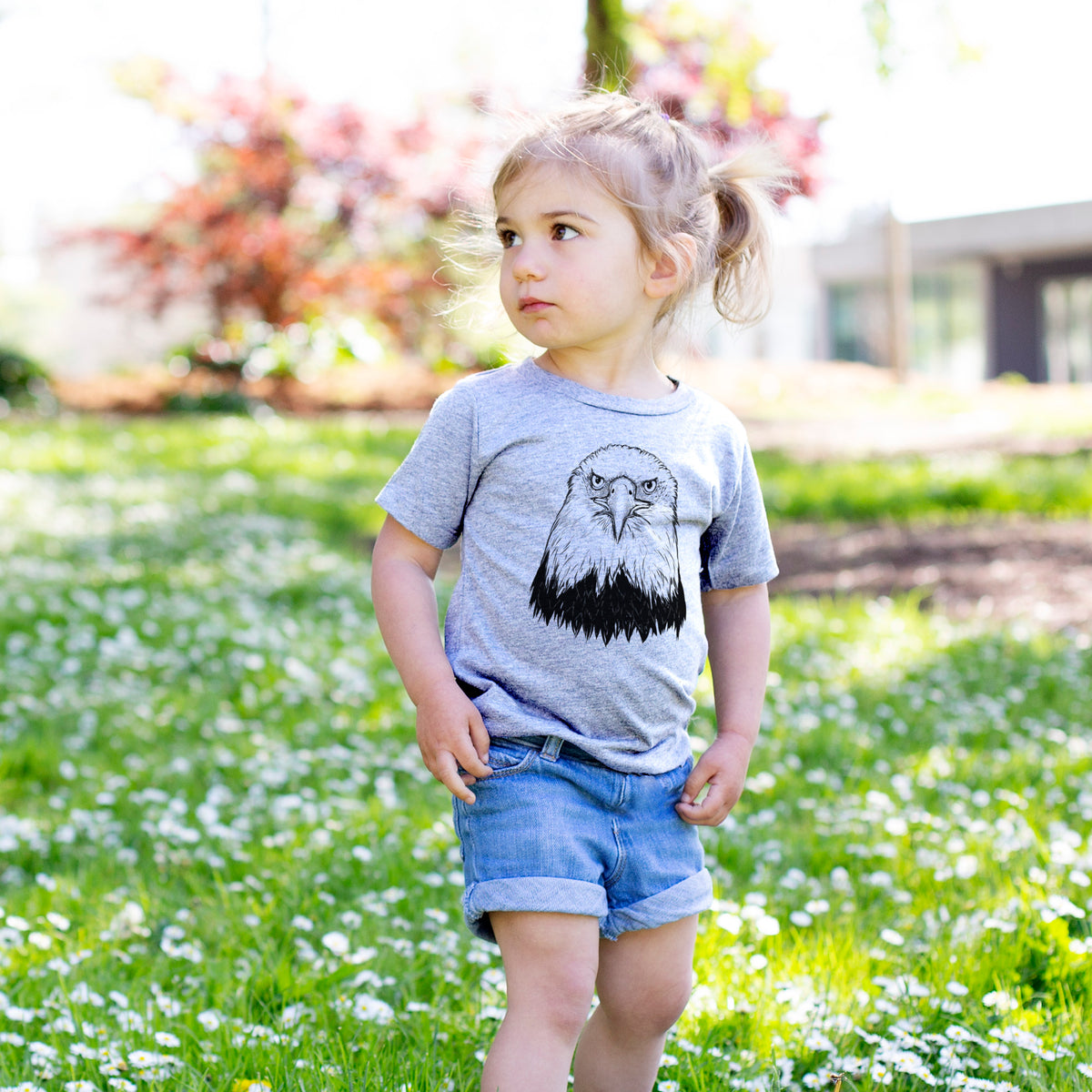 Toddler girl walking outdoors wearing a t-shirt printed with a detailed black ink portrait of a bald eagle facing forward.