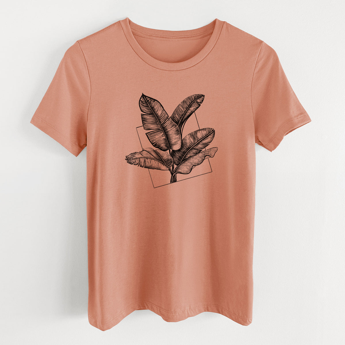 Terracotta orange women's relaxed fit cotton t-shirt laid flat, printed with a black ink illustration of banana leaves in front of a square outline.