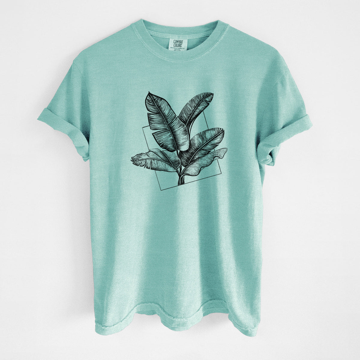 Chalky mint Comfort Colors t-shirt laid flat, printed with a black ink illustration of banana leaves in front of a square outline.